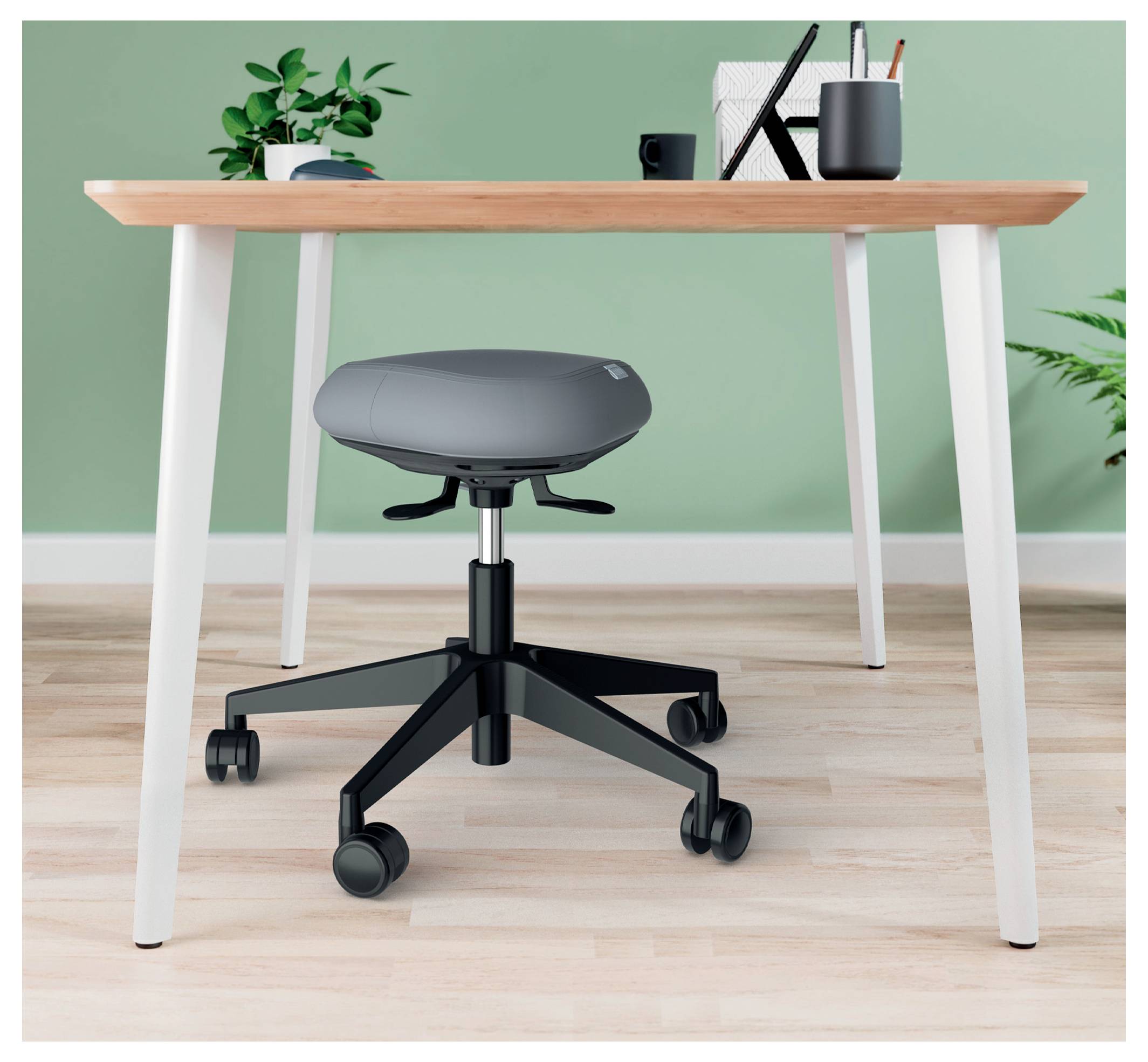 Egy modern, minimalista munkaállomás, benne egy fa asztal, kerekeken guruló szürke szék és zöld fal. Az asztalon alapvető felszerelési tárgyak, mint tollak és egy füzet vannak.