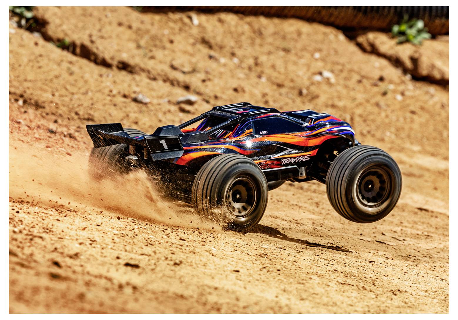 Egy távirányítós terepjáró autó robog végig egy poros pályán, port verve fel, ahogy gyorsan halad előre. Karosszériáján élénkpiros és sárga dizájnelemek láthatók.