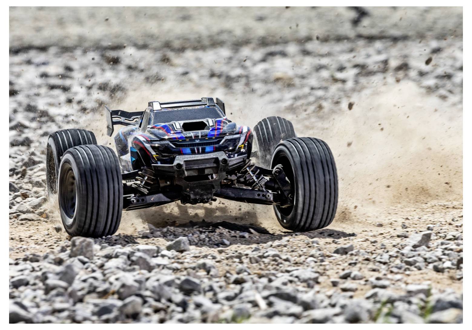 Egy távirányítású autó gyorsan halad egy sziklás terepen, port verve fel. Az autó nagy kerekekkel és áramvonalas dizájnnal rendelkezik.