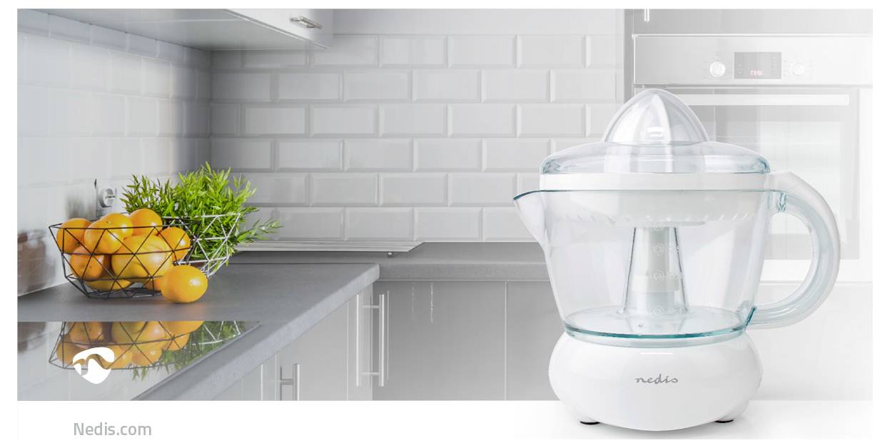 Egy átlátszó citrusprés áll egy modern konyhapulton egy drótkosár mellett, amely narancsokkal és zöld fűszernövényekkel van tele.