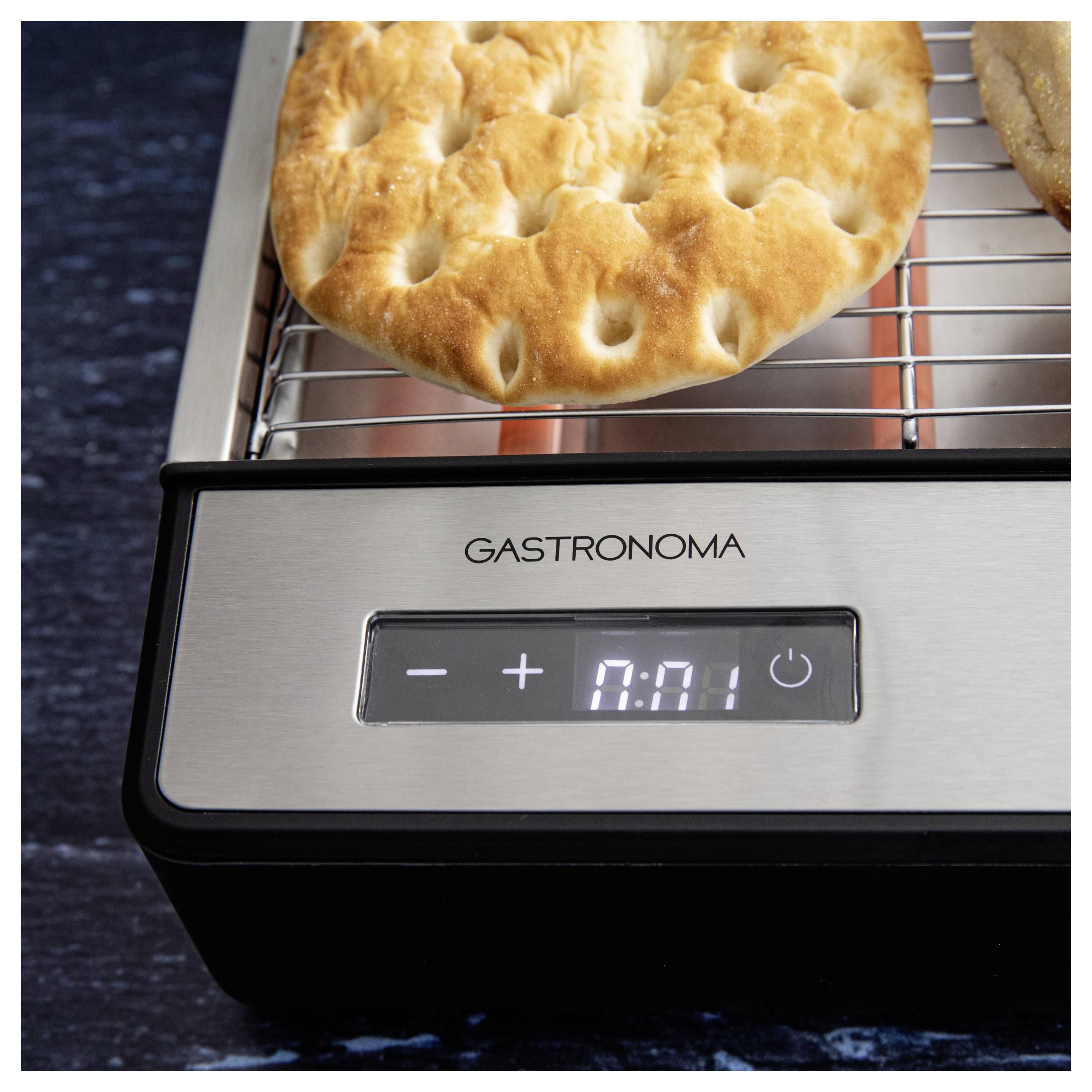 Egy lyukacsos kenyérlepény pirul egy elektromos grillsütőn, amelynek digitális kijelzőjén '0:01' látható.