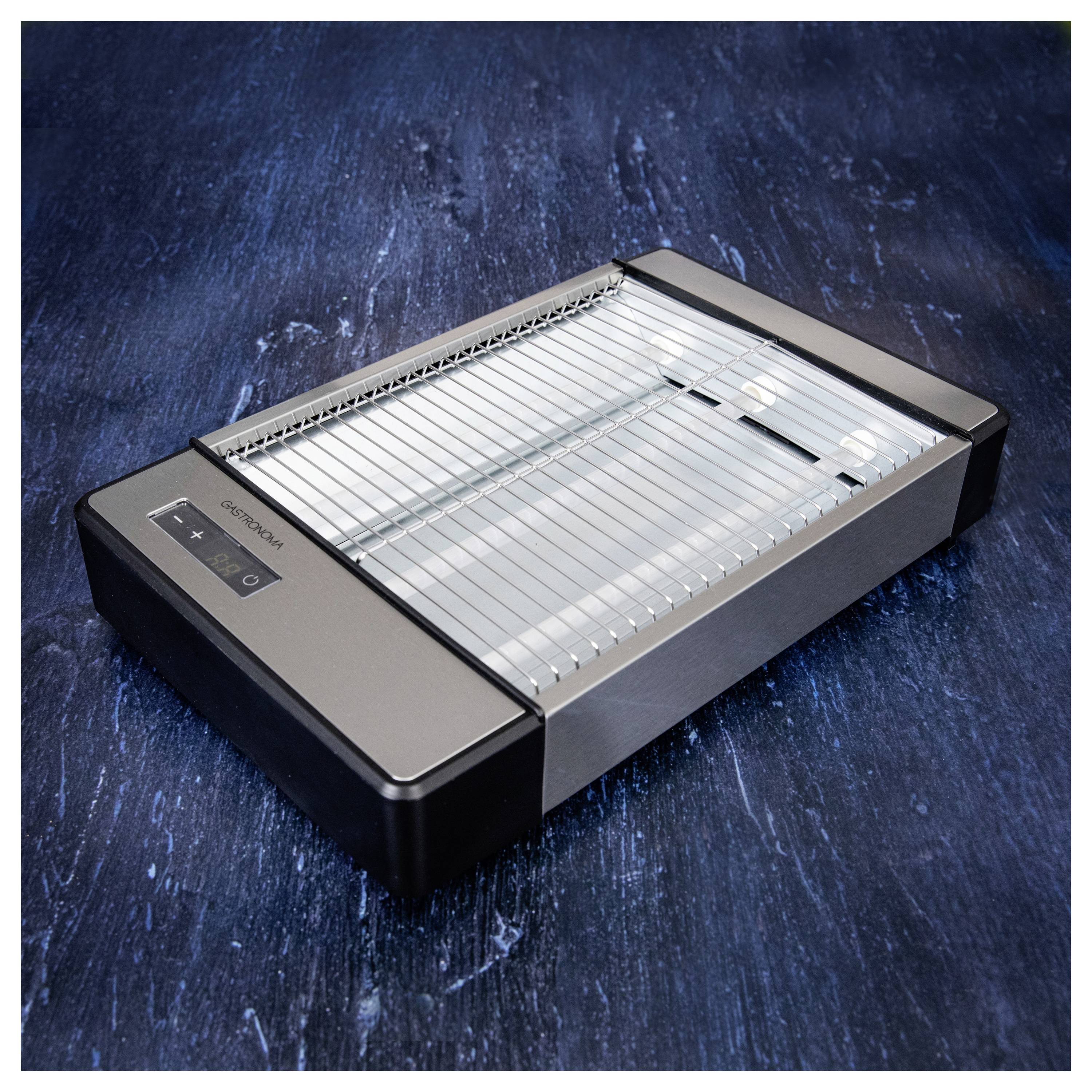 Egy rozsdamentes acél elektromos grillsütő digitális vezérlőpanellel és tökéletesen sima formatervezéssel, sötét textúrájú felületen elhelyezve.