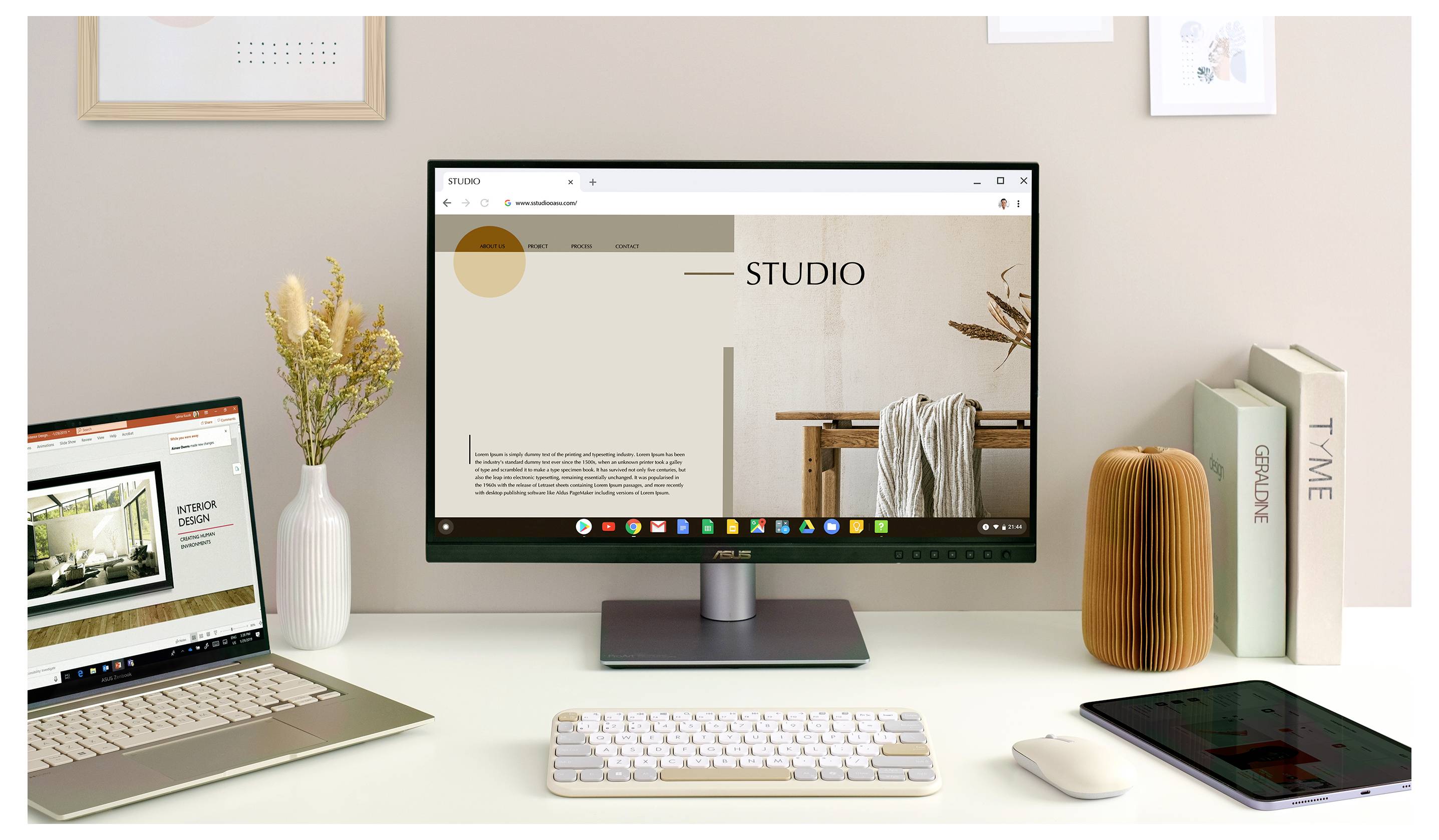 Egy modern munkahely egy asztali monitorral, amelyen egy 'STUDIO' weboldal látható, egy laptop, egy billentyűzet, dekoratív tárgyak és könyvek.