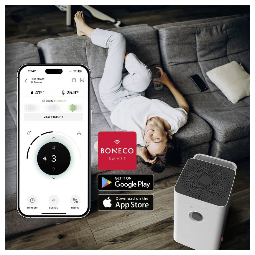 Egy nő egy kanapén pihen, kezében egy okostelefon, amelyen a 'Boneco Smart' légtisztító alkalmazás látható, légminőségi adatokkal és beállításokkal. A közelben egy légtisztító készülék áll.
