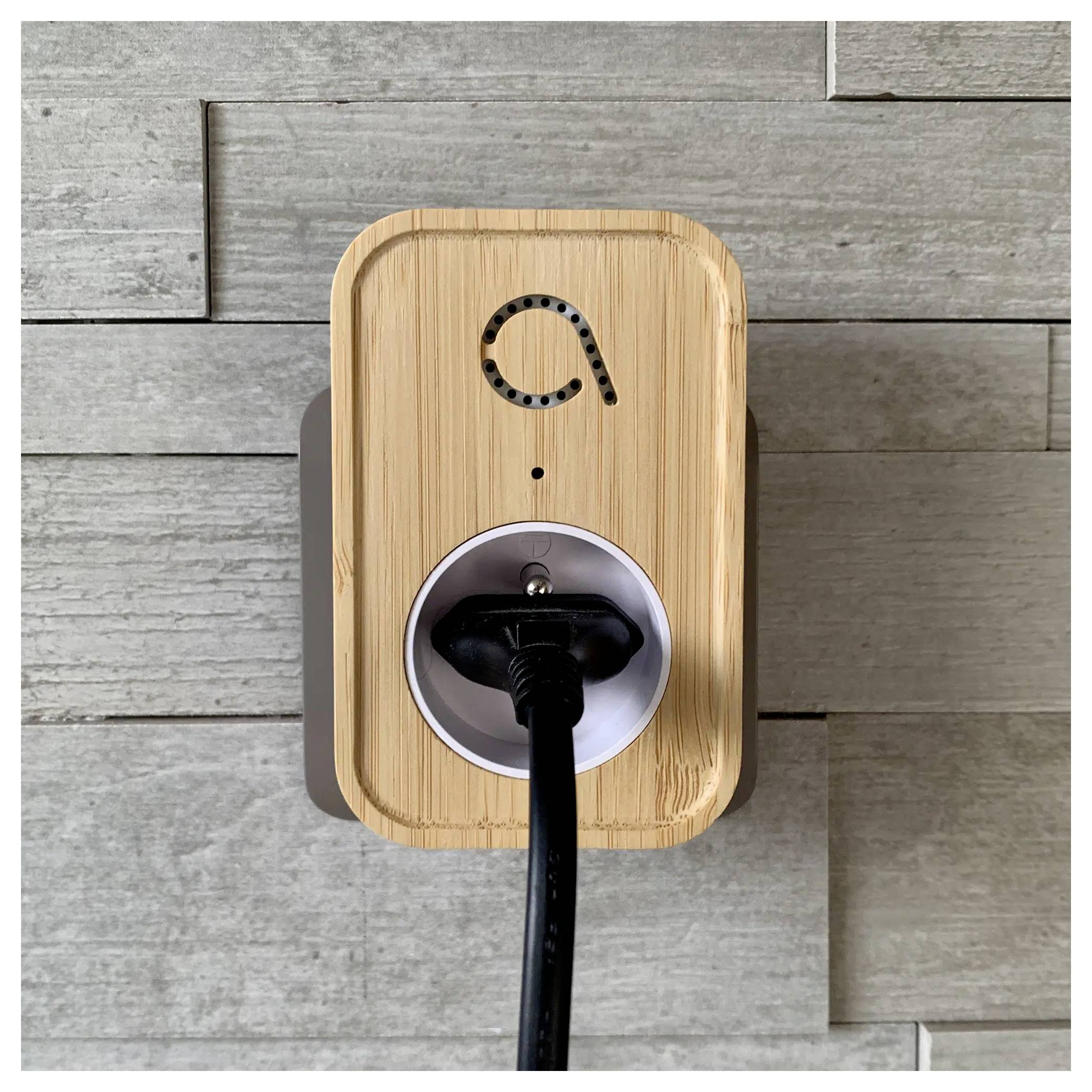 Egy fa mintázatú okos konnektor szürke csempés falon, fekete kábellel bedugva a foglalatába, amelyen áramellátás ikon látható.