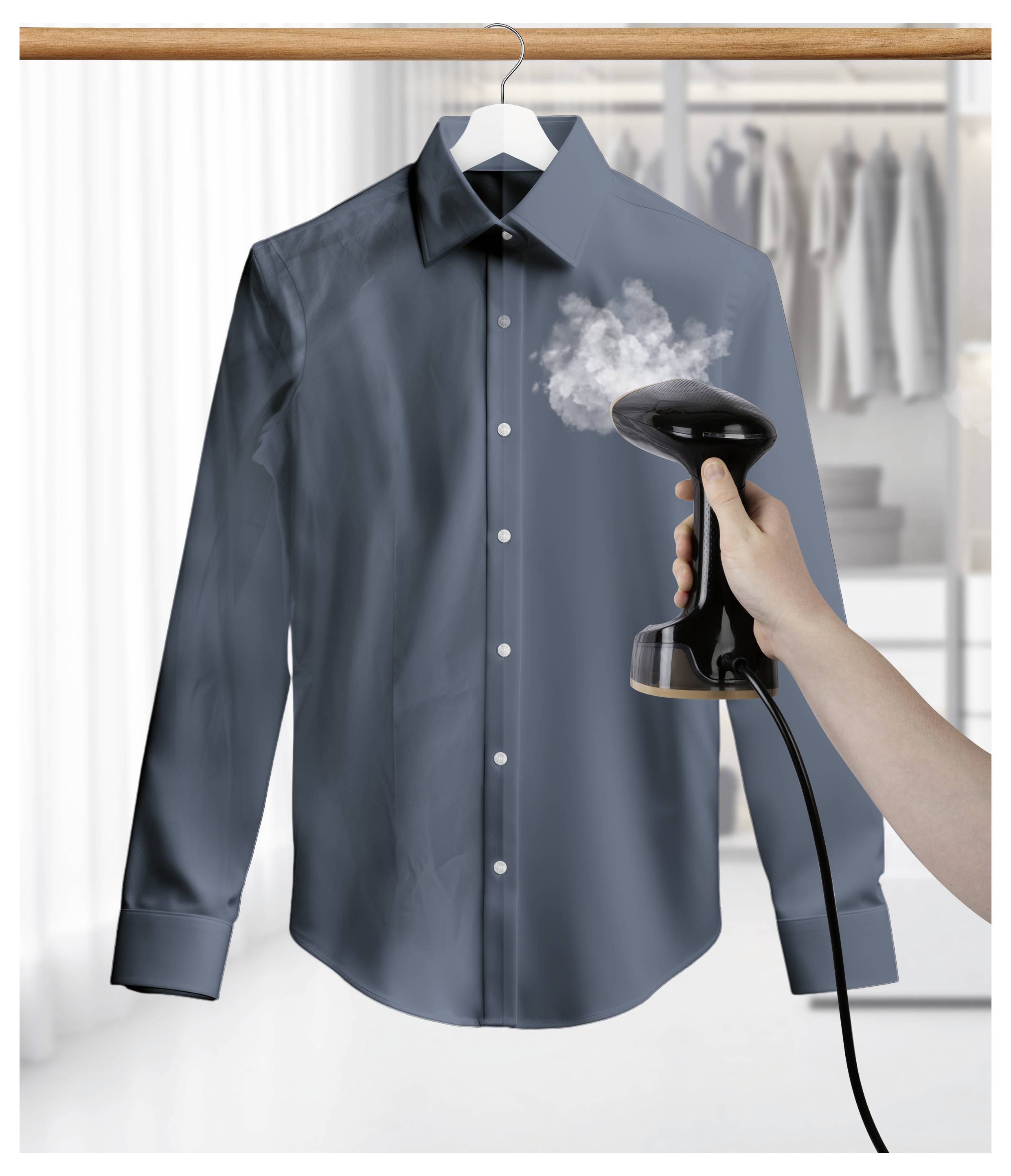 Egy kéz gőzölőt használ a sötét ing ráncainak eltávolítására, amely egy akasztón lóg, a háttérben elmosódott gardróbbal.