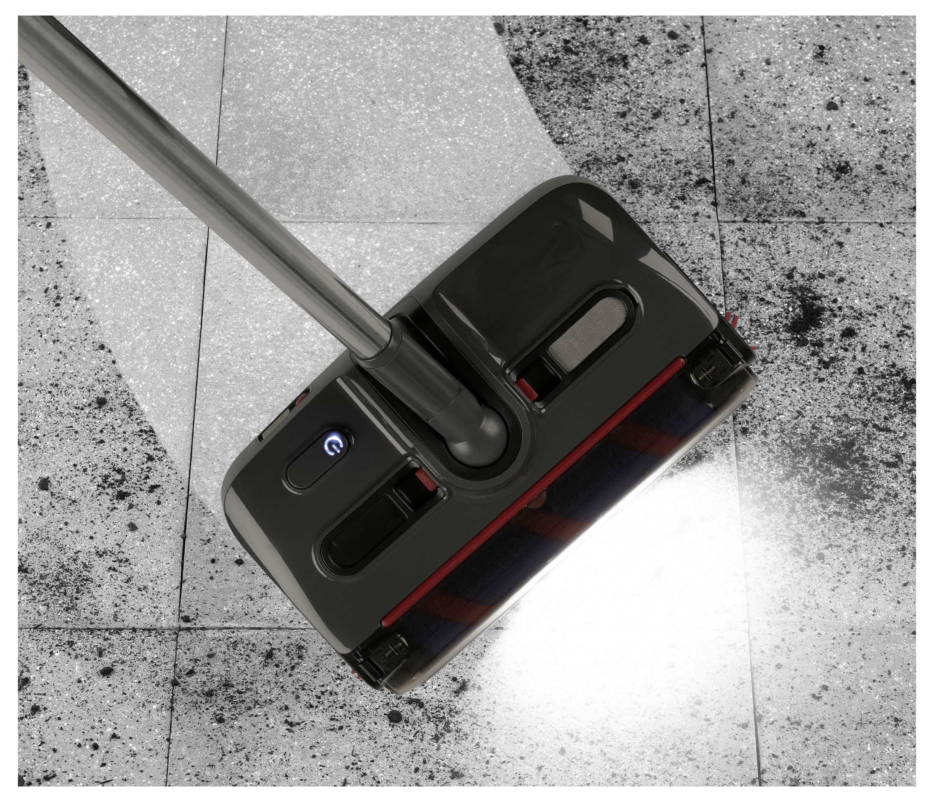 Egy padlótisztító gép használatban, por és szennyeződést söpör egy csempézett padlóról, tiszta nyomot hagyva maga után.