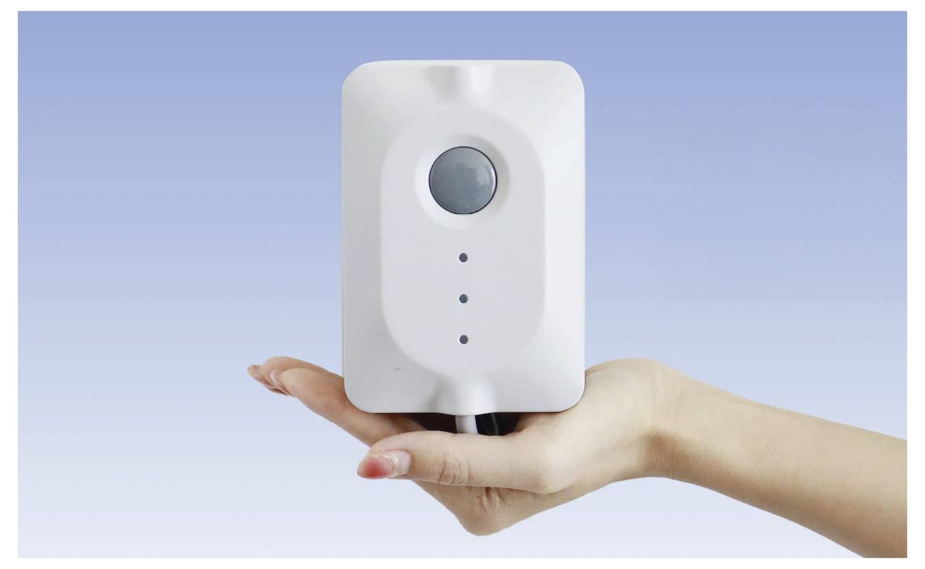 Egy kéz egy fehér eszközt tart, amelyen egy kör alakú gomb és három kis jelzőfény található, kék gradiens háttér előtt.