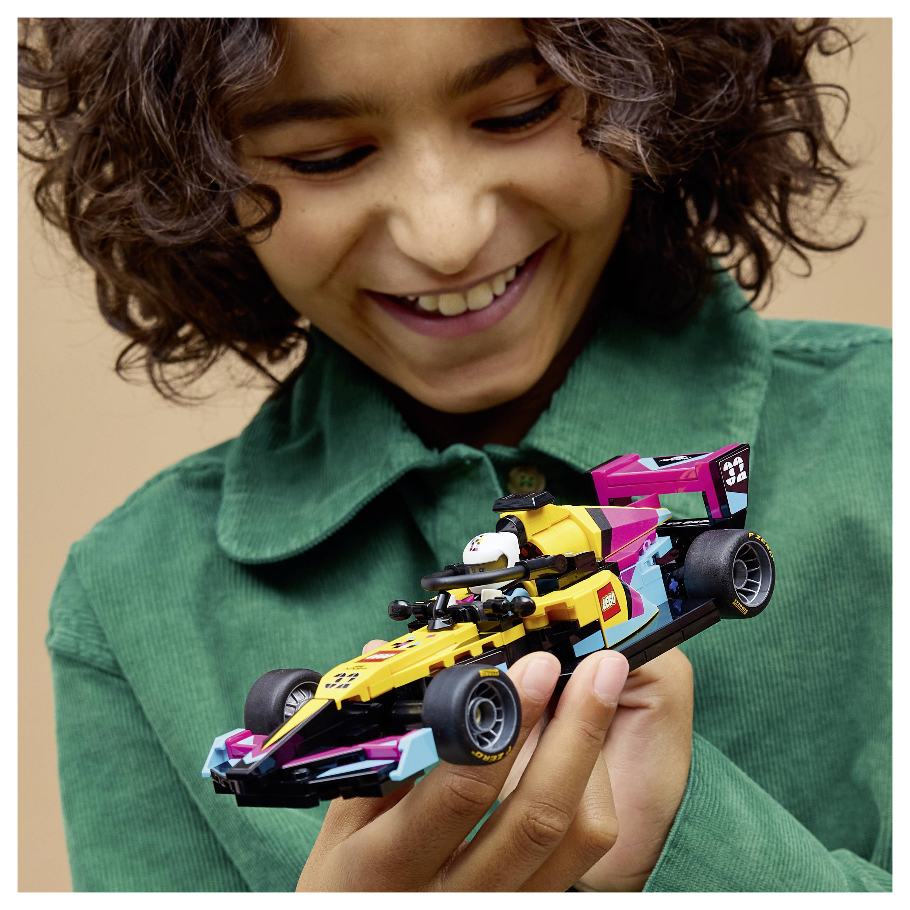 Egy gyermek egy színes játék versenyautót tart a kezében, boldogan mosolyog és izgatottan vizsgálgat a részletgazdag modellt.