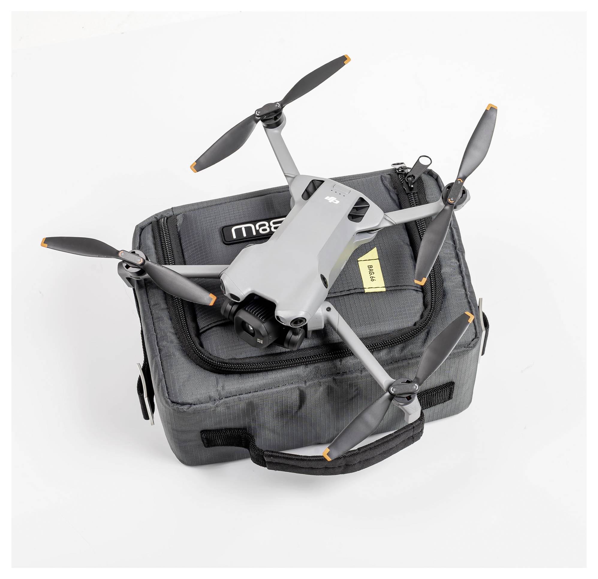 Egy kompakt, szürke drón négy propellerrel egy szürke hordtáskán pihen. A táskának fekete fogója van és egy látható címkéje.