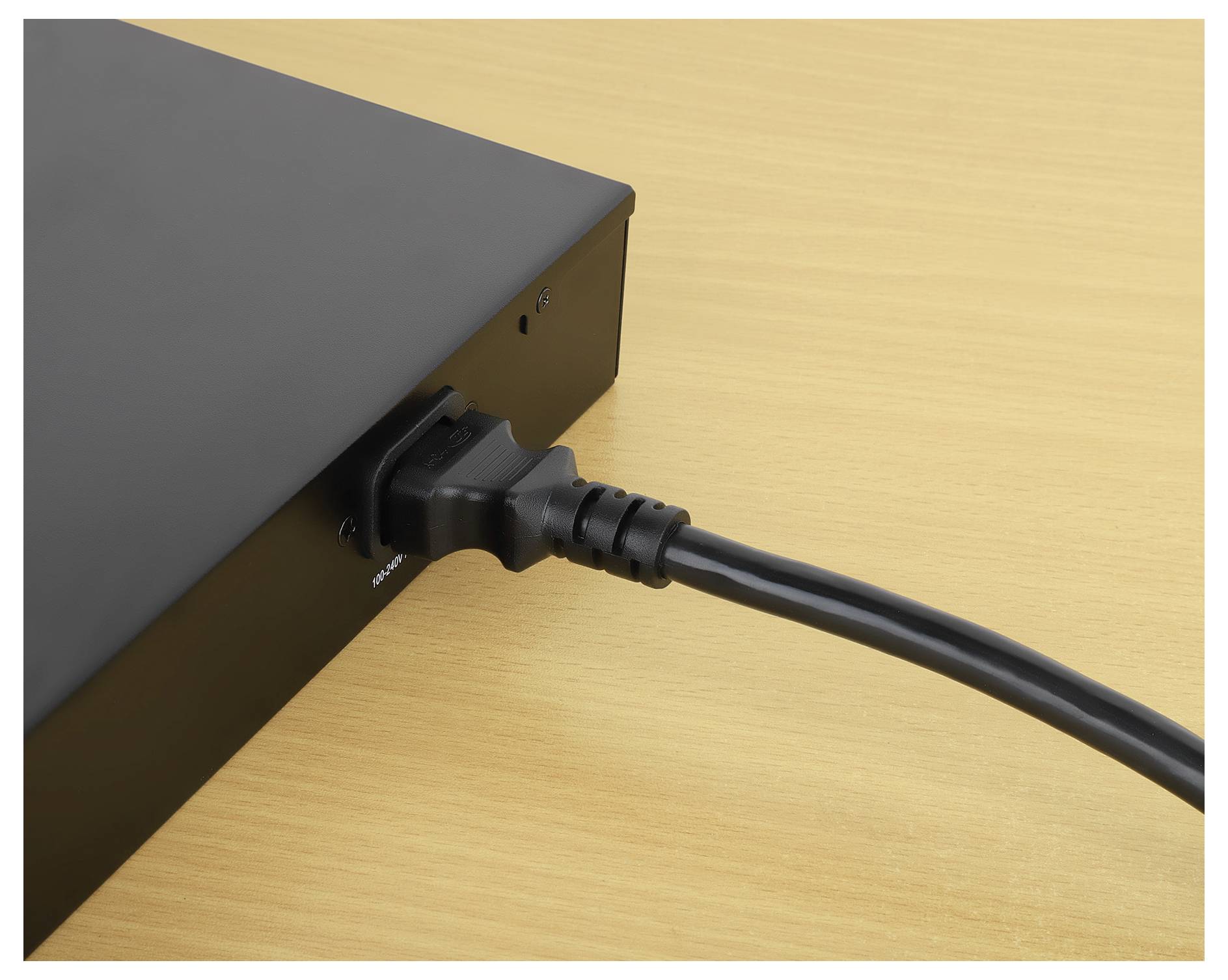 Fekete tápkábel egy elektronikus eszközbe bedugva egy faalapú felületen.