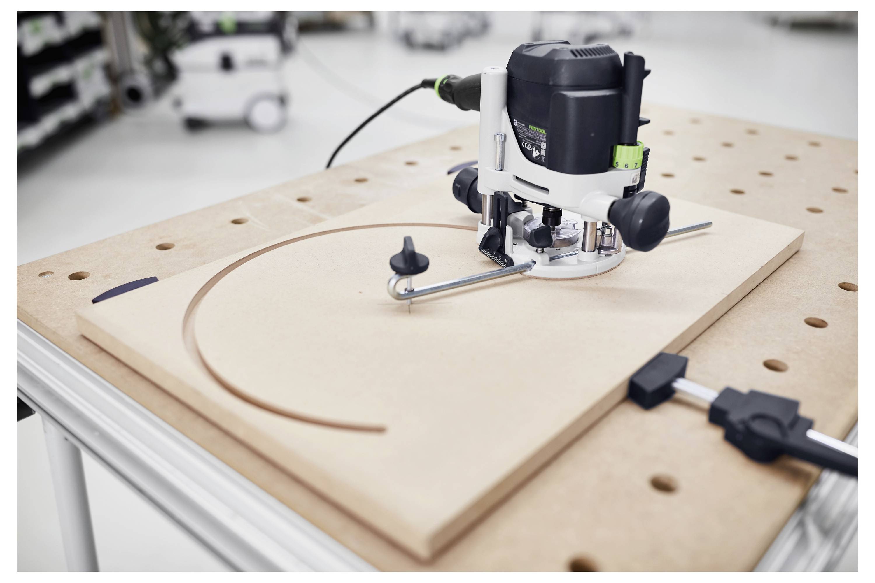 Egy munkapad tetején lévő marógép ívelt hornyot vág egy fadeszkába, egy fém vezető által szabályozott precíziós megmunkáláshoz.