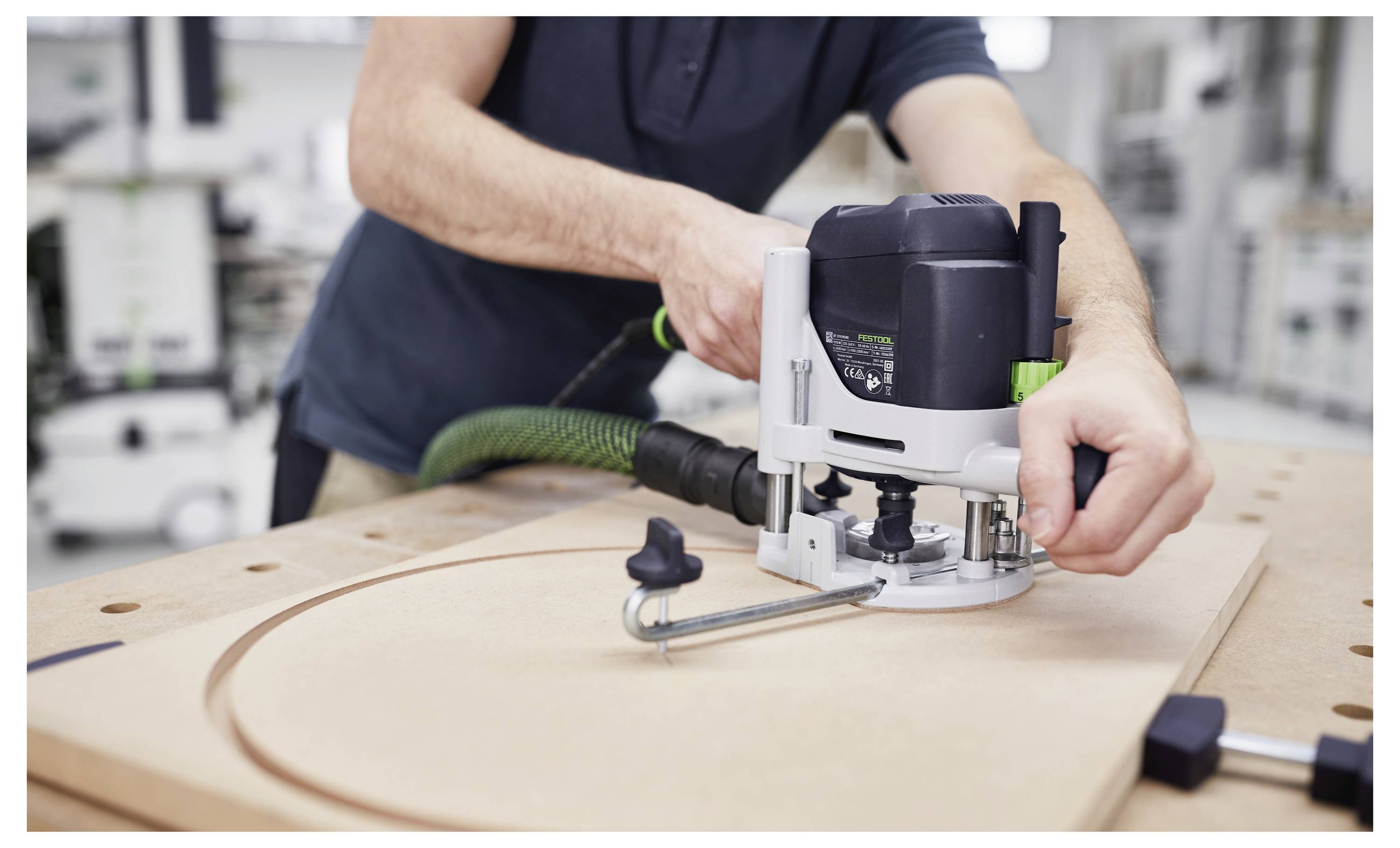 Egy munkaasztalra szerelt Festool marógép egy fadarabot vág egy műhelyben, porelnyelő rendszerhez csatlakoztatott szívócső mellett.