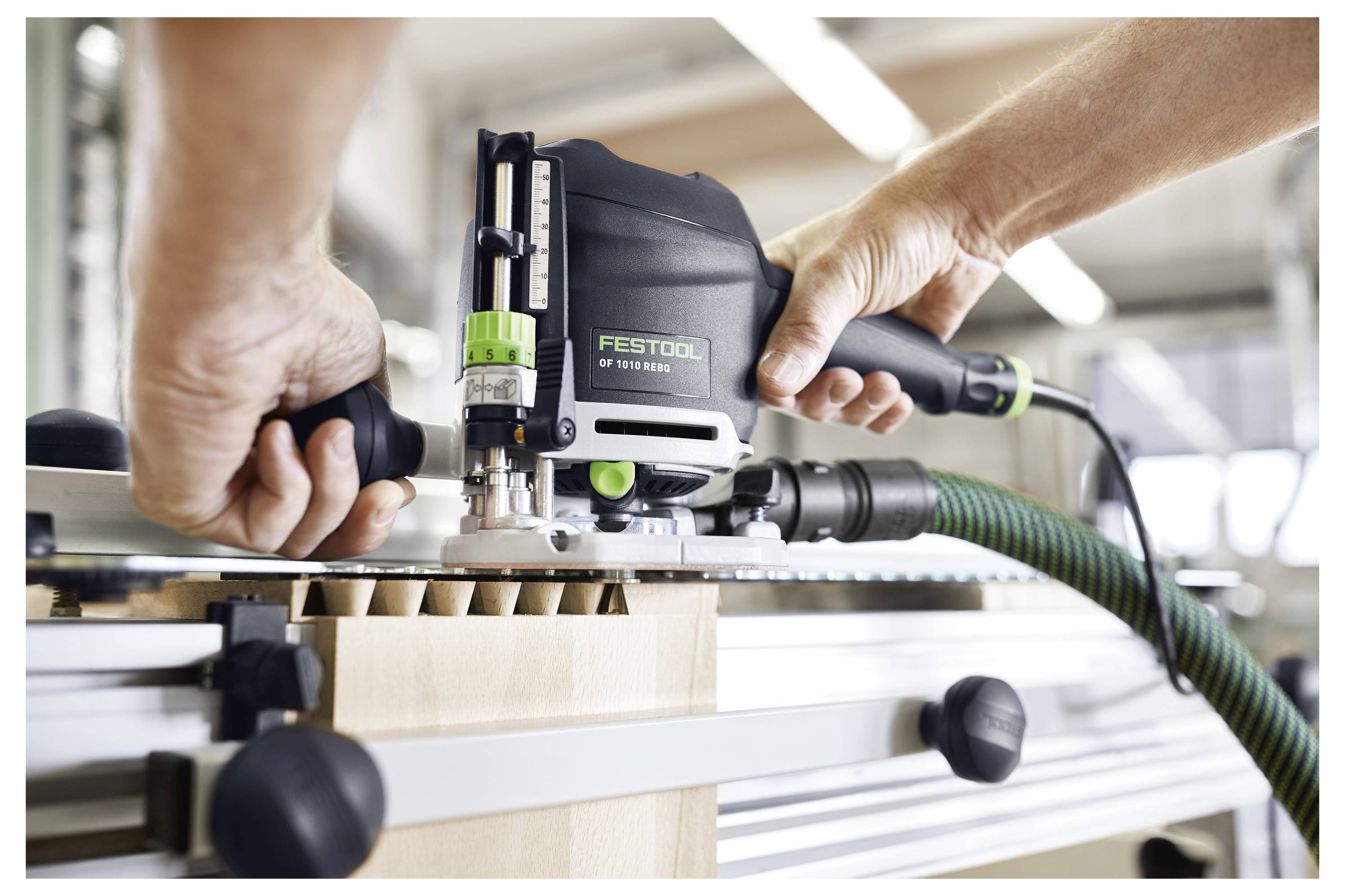 Kezek egy Festool elektromos szerszámot üzemeltetnek, egy ipari műhelyben pontosan hornyokat vágnak egy fadarabba.