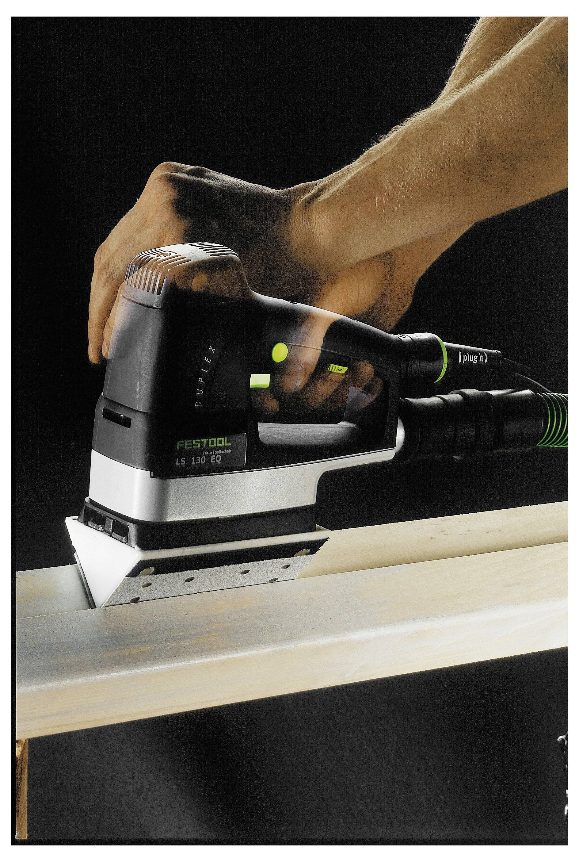 Egy személy Festool csiszolót használ egy fadeszkán, simítva annak felületét. A kép az eszközre és a kéz mozgására összpontosít.