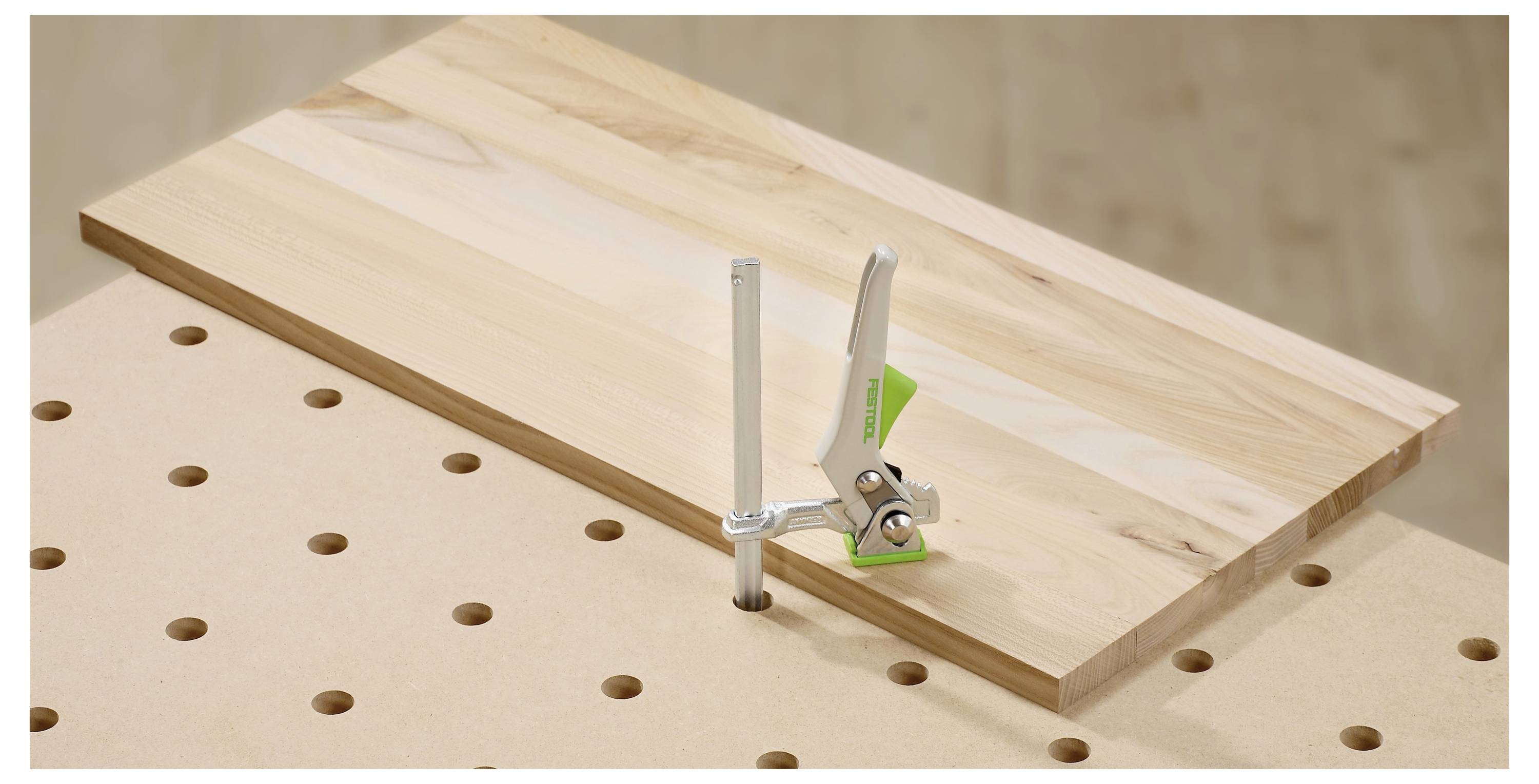 Egy személy zöld és fekete elektromos fúrót használ egy fa felületen egy műhelyszerű környezetben.