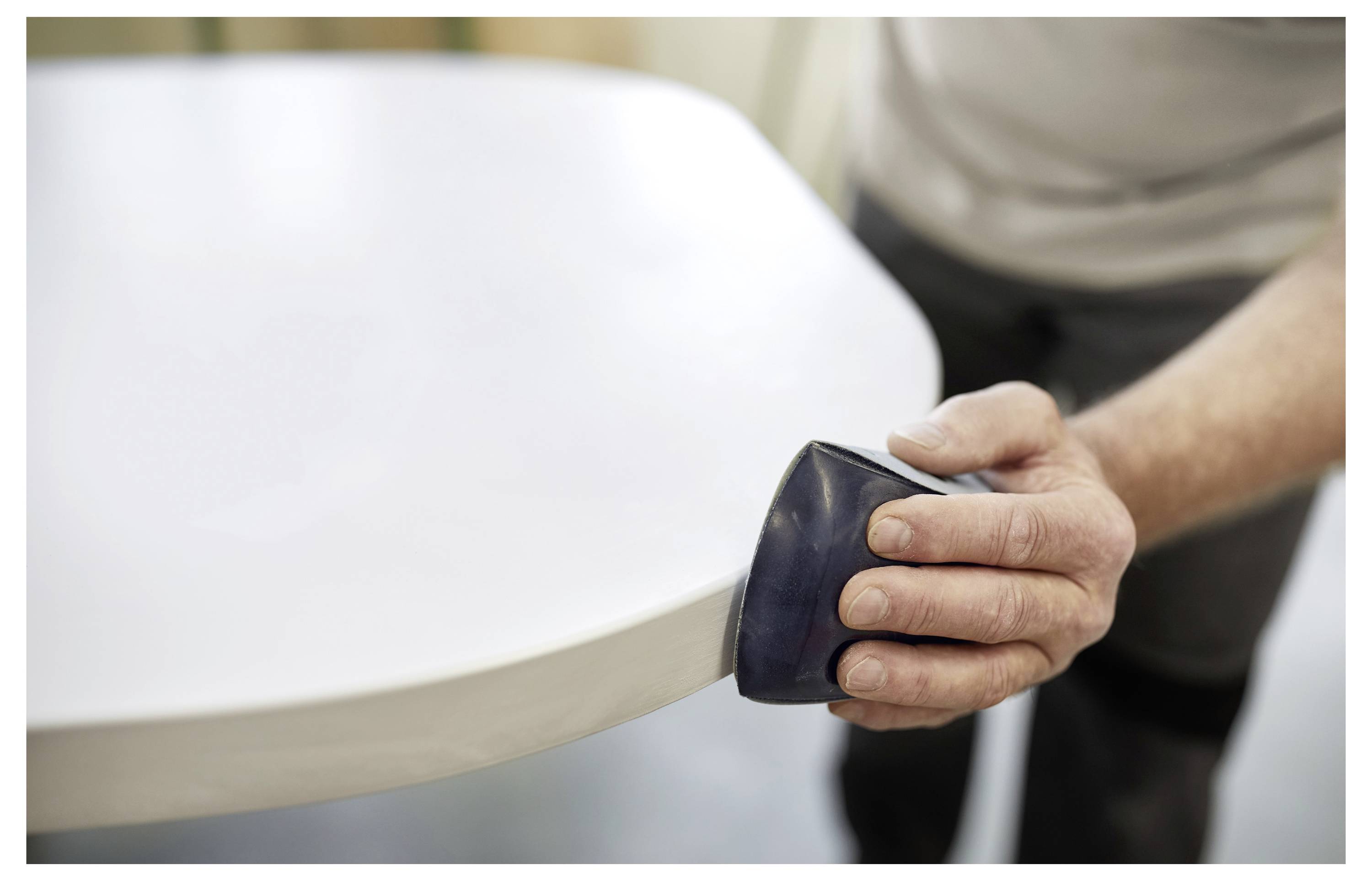 Egy személy egy fehér asztal szélét csiszolja csiszolóhasábbal, a felület simítására összpontosítva.