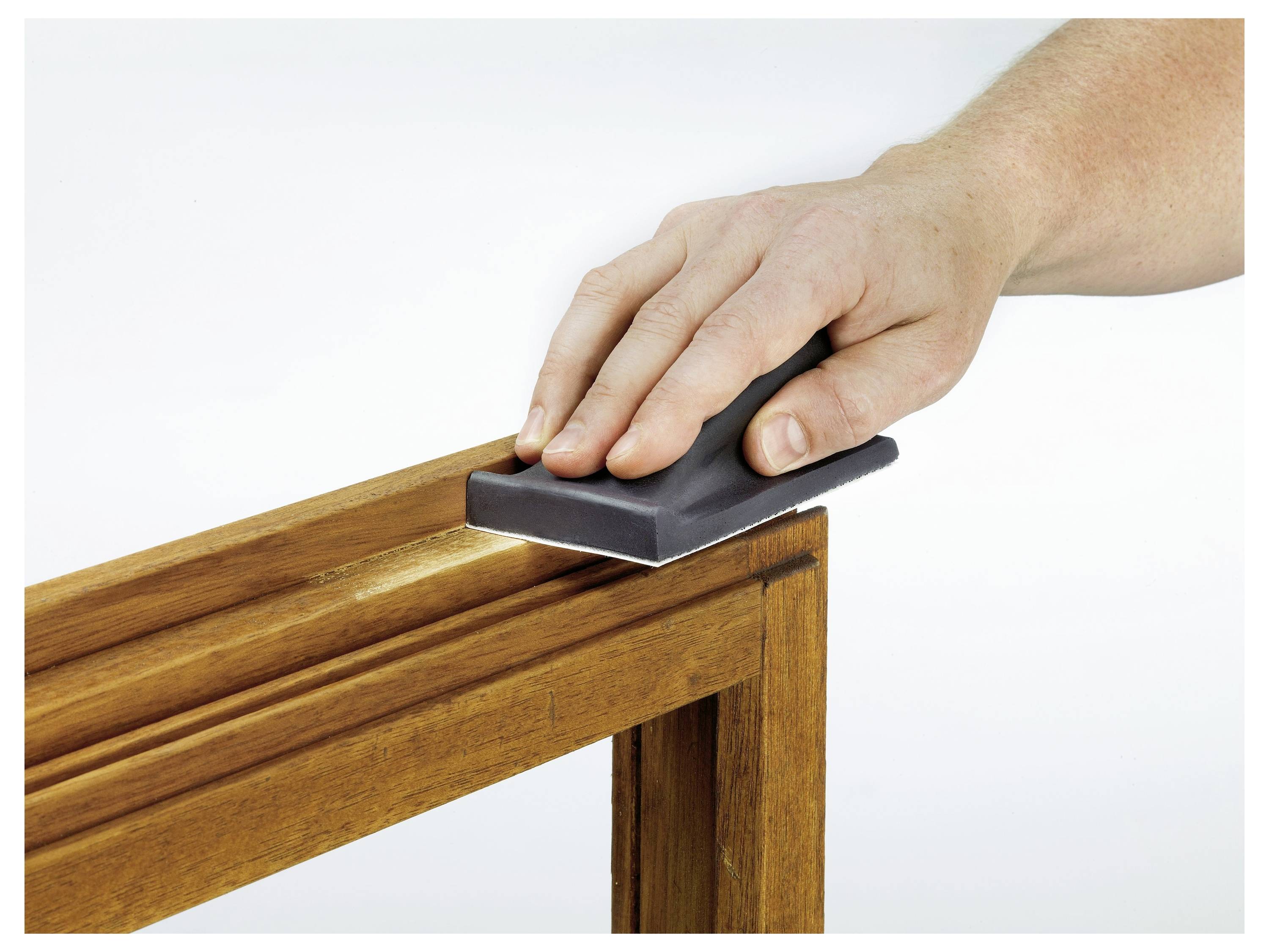 Egy kéz egy fafenék szélét csiszolja csiszolóblokkkal, bemutatva a fafelületek simítási folyamatát.