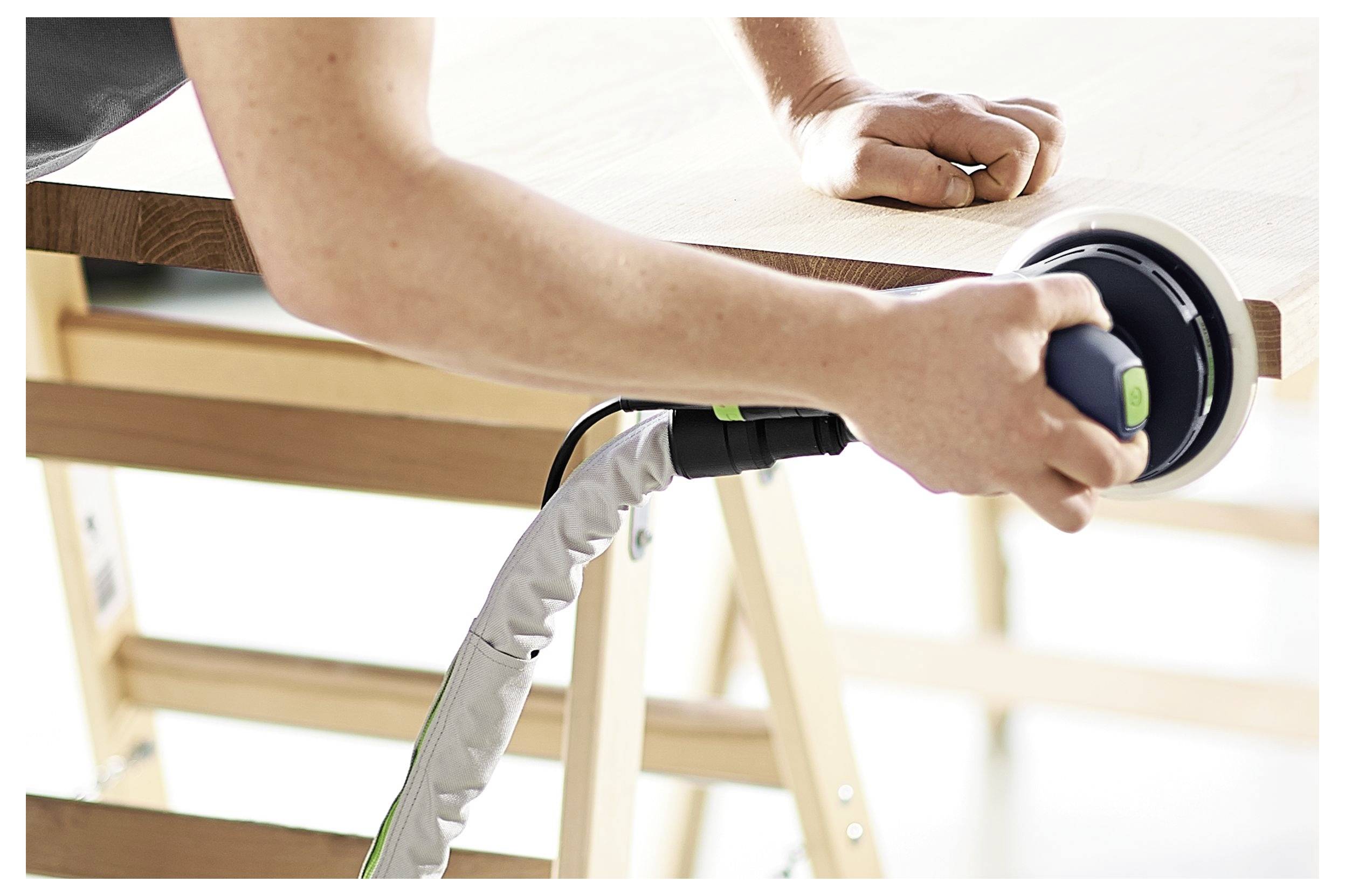 Egy személy elektromos csiszolóval csiszol fa felületet egy asztalon, a felület simítására koncentrálva, műhelykörnyezetben.