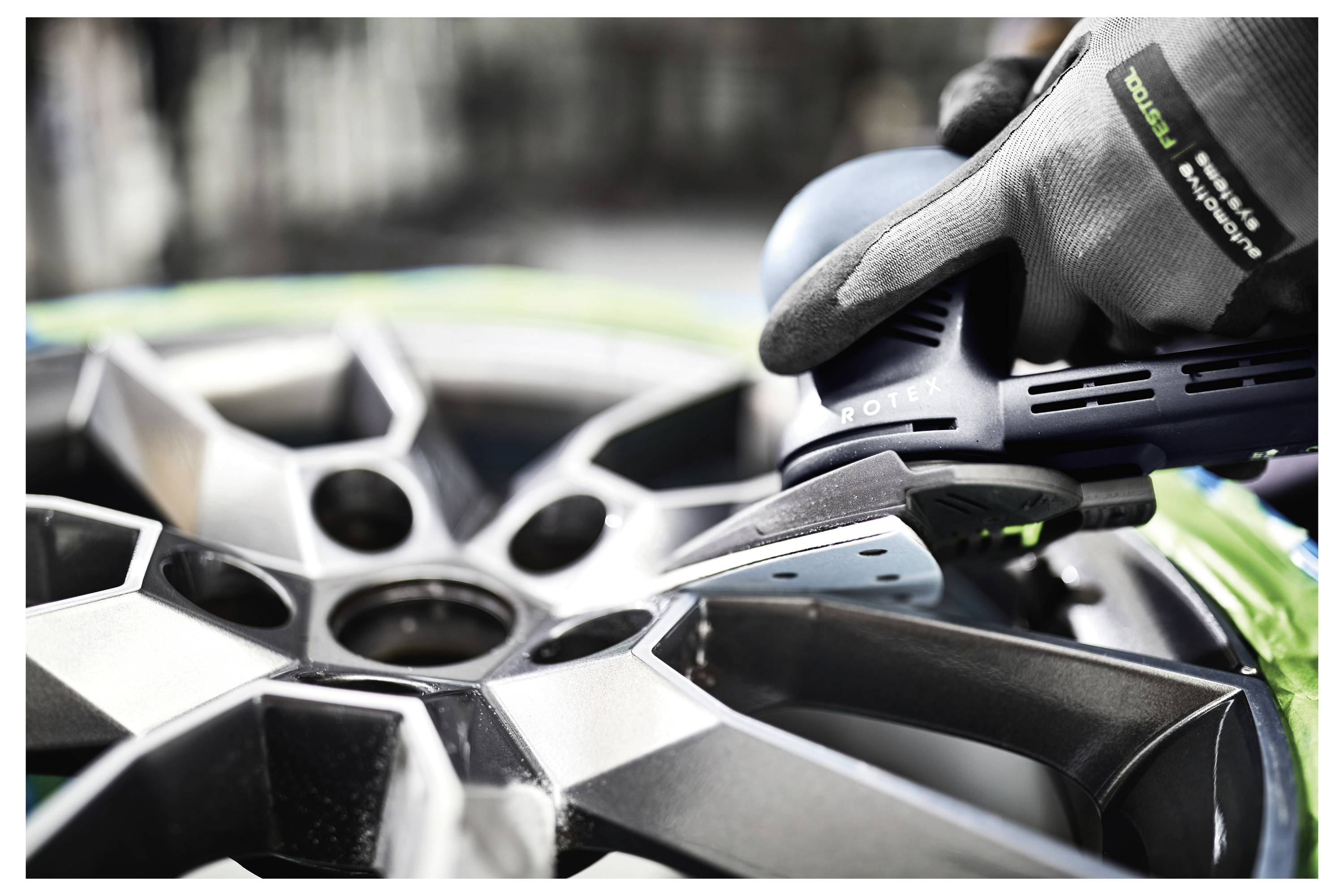 Egy személy védőkesztyűt viselve csiszolószerszámot használ egy ezüst autókerékre.