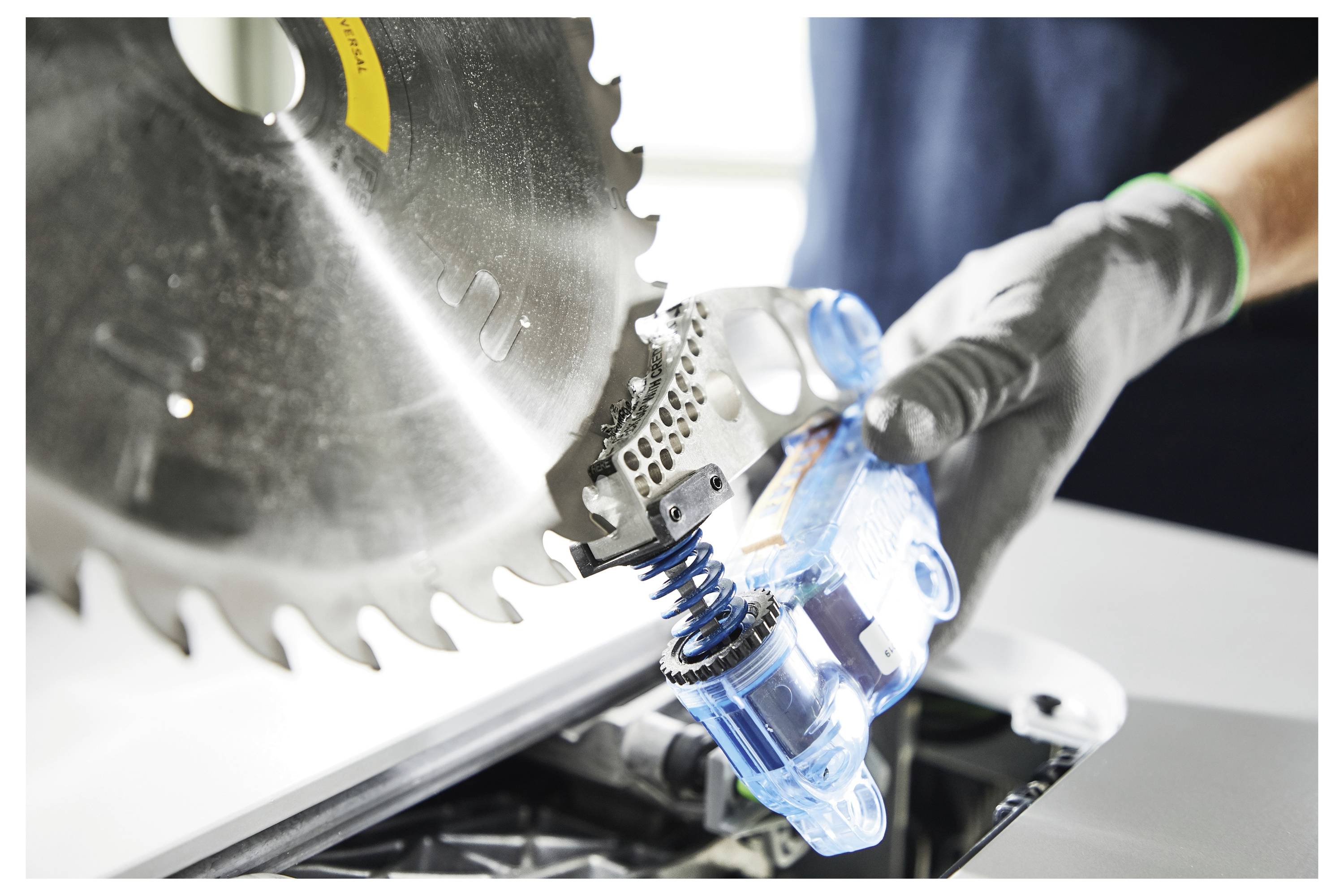 Egy biztonsági felszerelésben lévő személy elektromos fűrésszel vágja a fadeszkákat, fűrészpor száll a levegőben egy modern műhelyben.