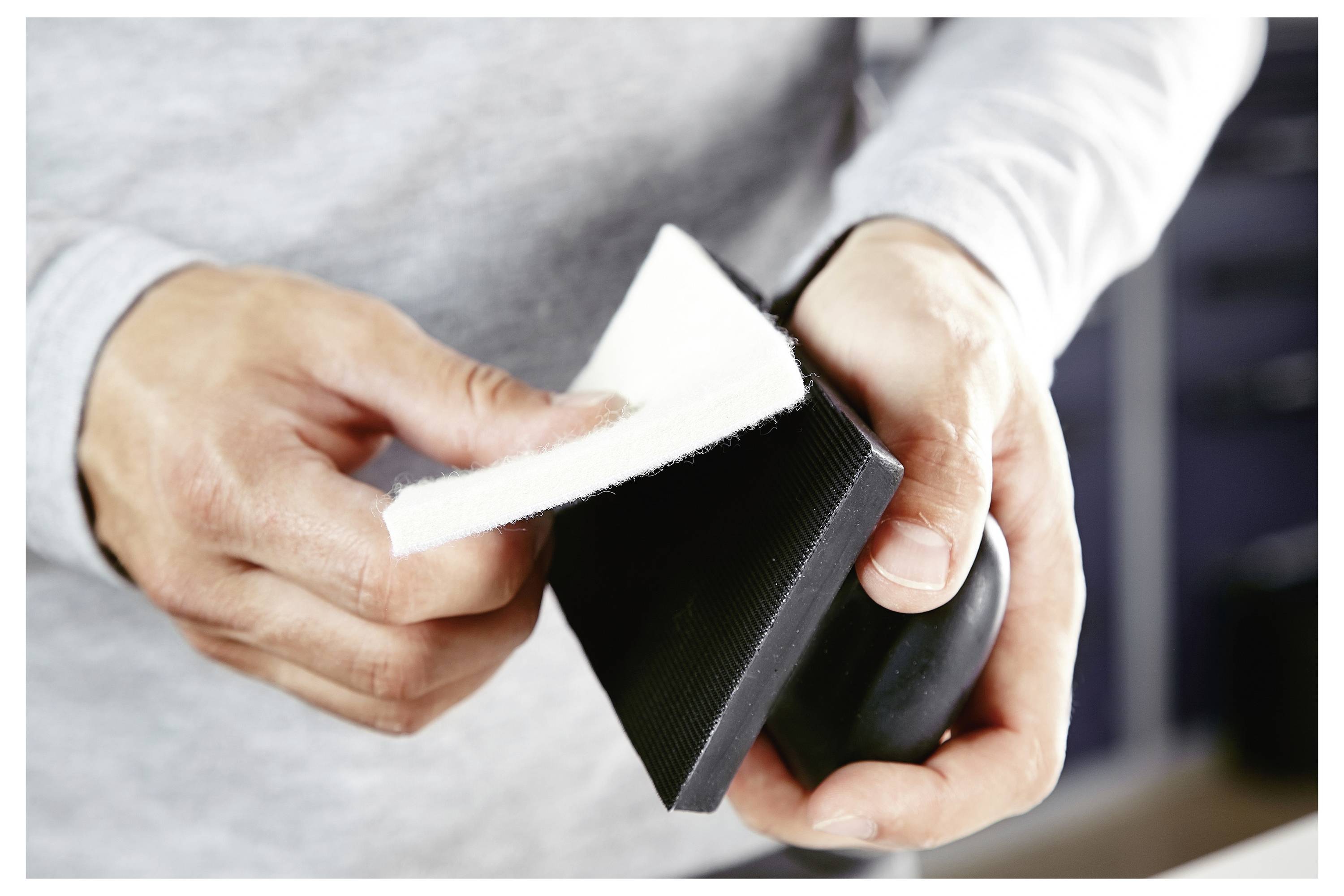 Egy személy csiszolóhasábot és csiszolópapírt tart, egy felület simításához készülődik.