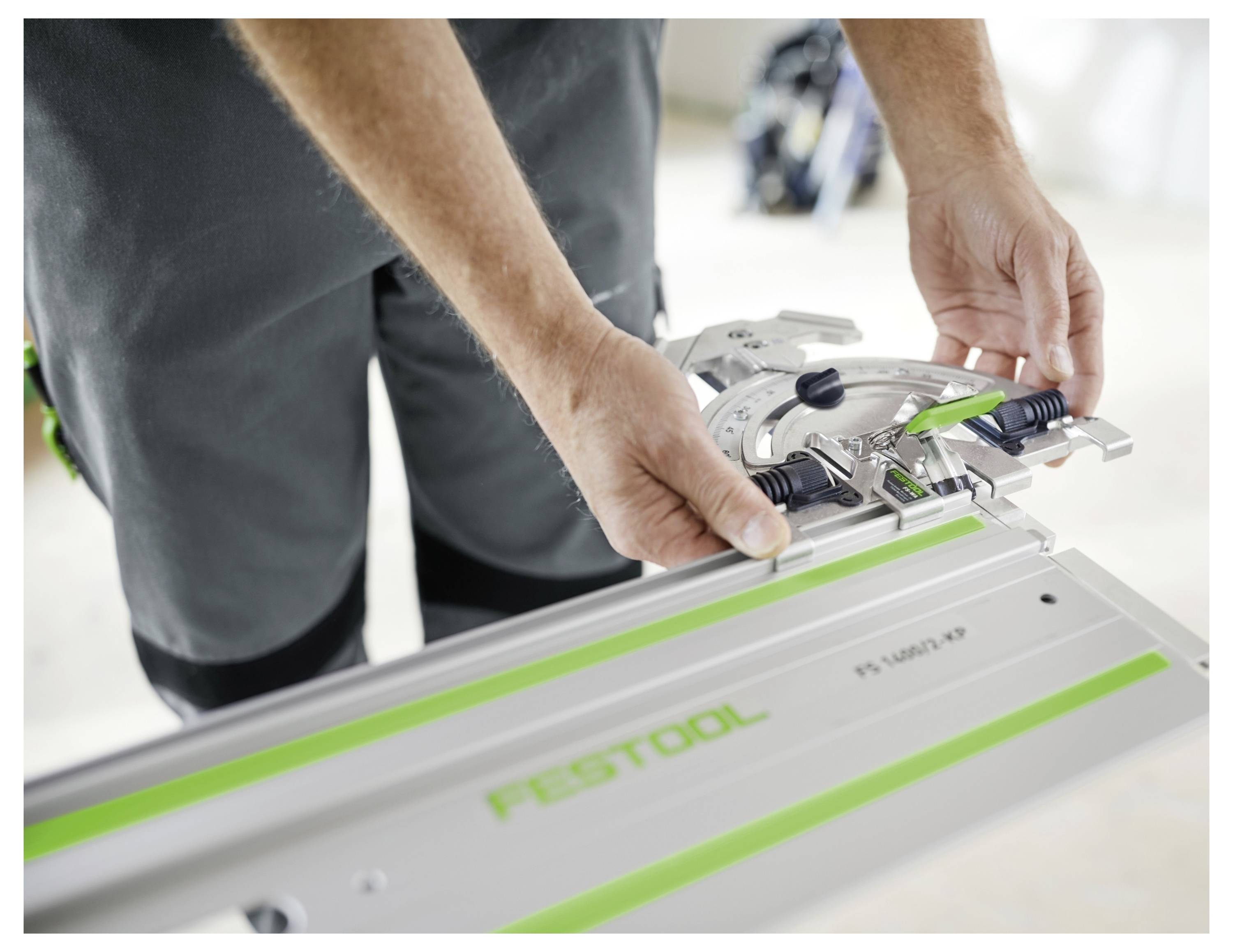 Egy személy Festool vezetőléc-rendszerét állítja be közeletimagba, a képen a kezek láthatóak, ahogy rögzítik a vezetőlécet a pontos vágáshoz.