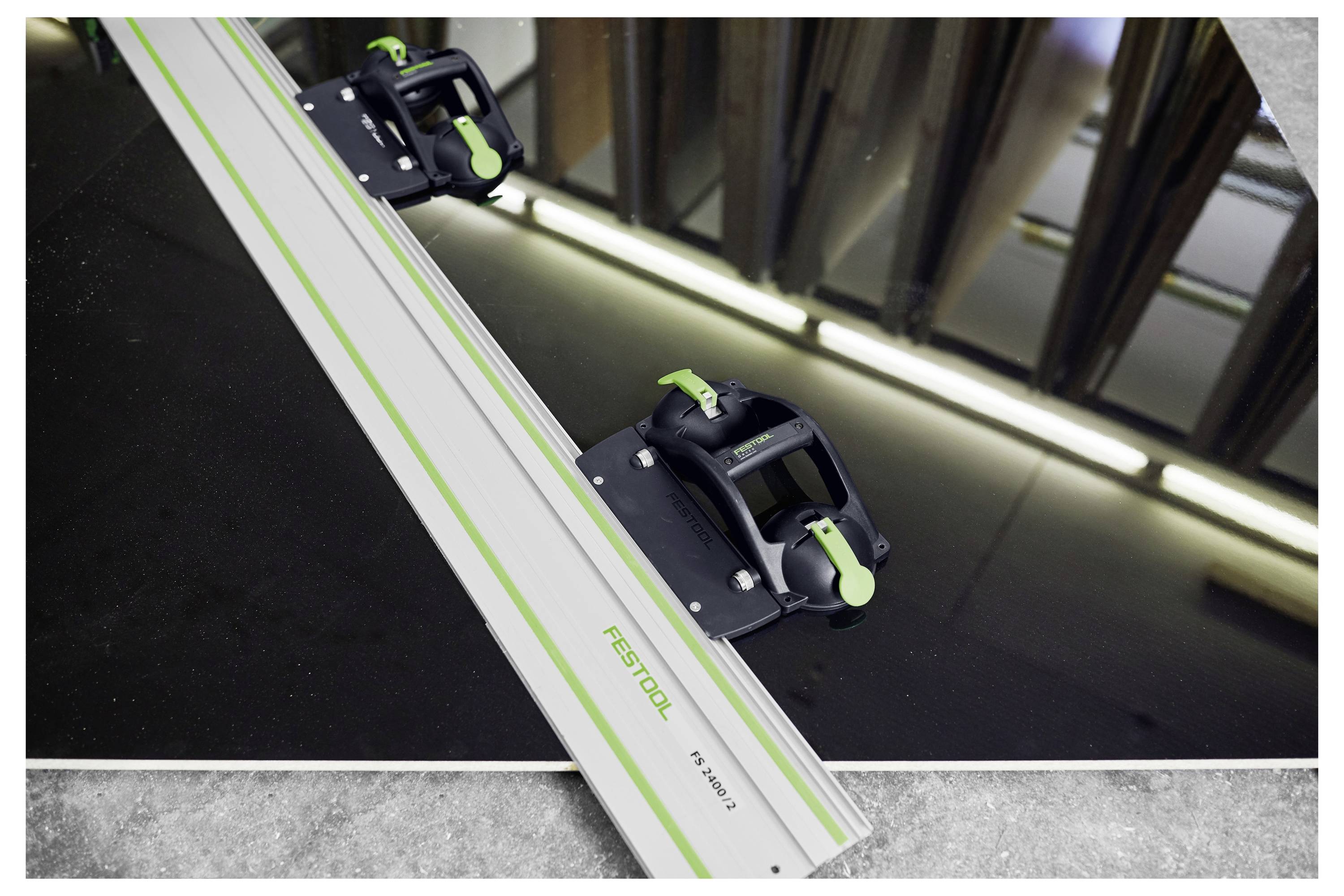Egy zöld kiegészítésekkel rendelkező fém vezetősín, amely a "Festool" márkával van ellátva, egy fénylő sötét felületre van igazítva egy műhelykörnyezetben.