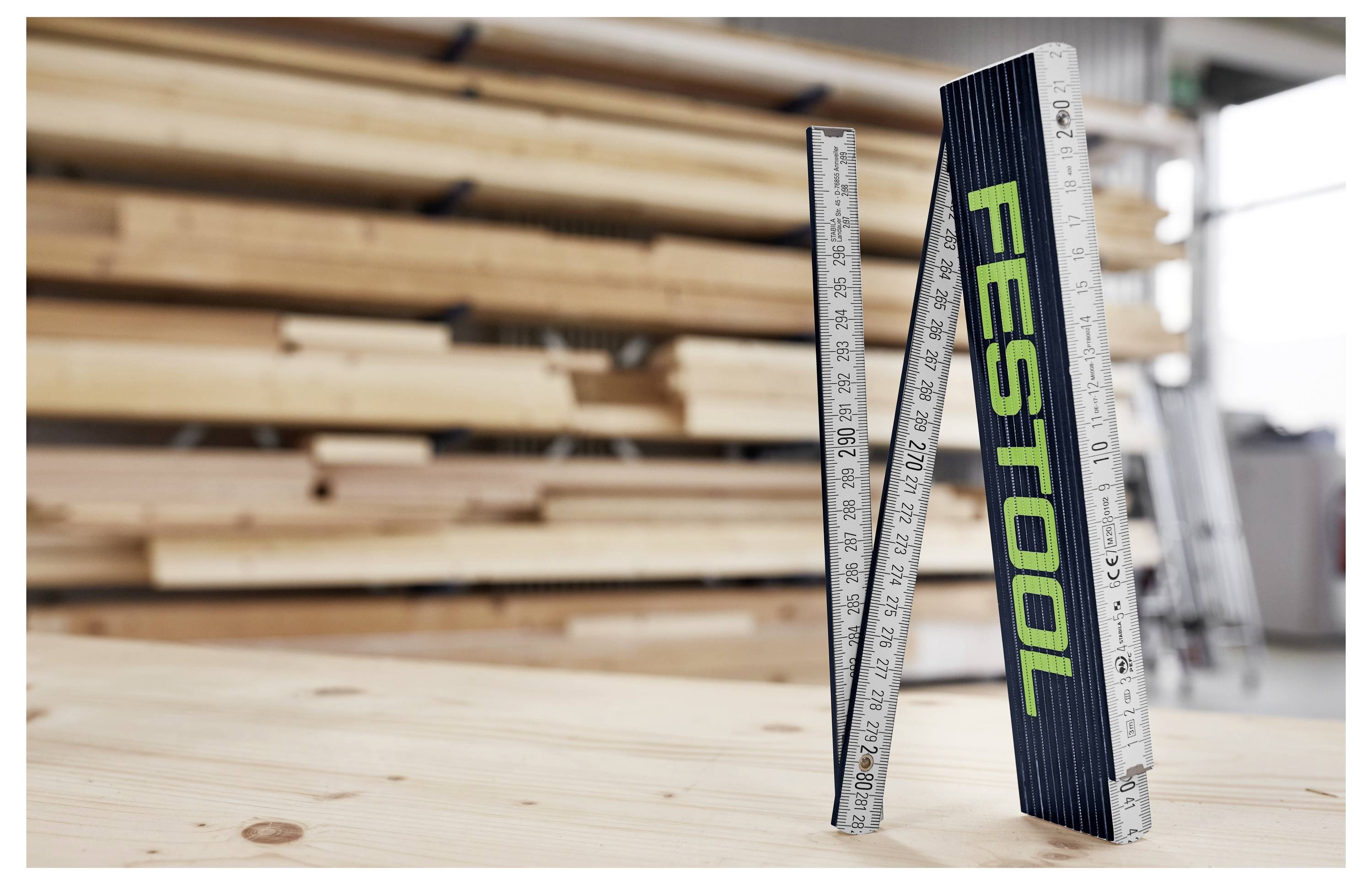 Személy elektromos fúrógépet használva festék keverésére egy építési helyszínen, kesztyűt és védőruházatot viselve, a háttérben kitett téglafallal.