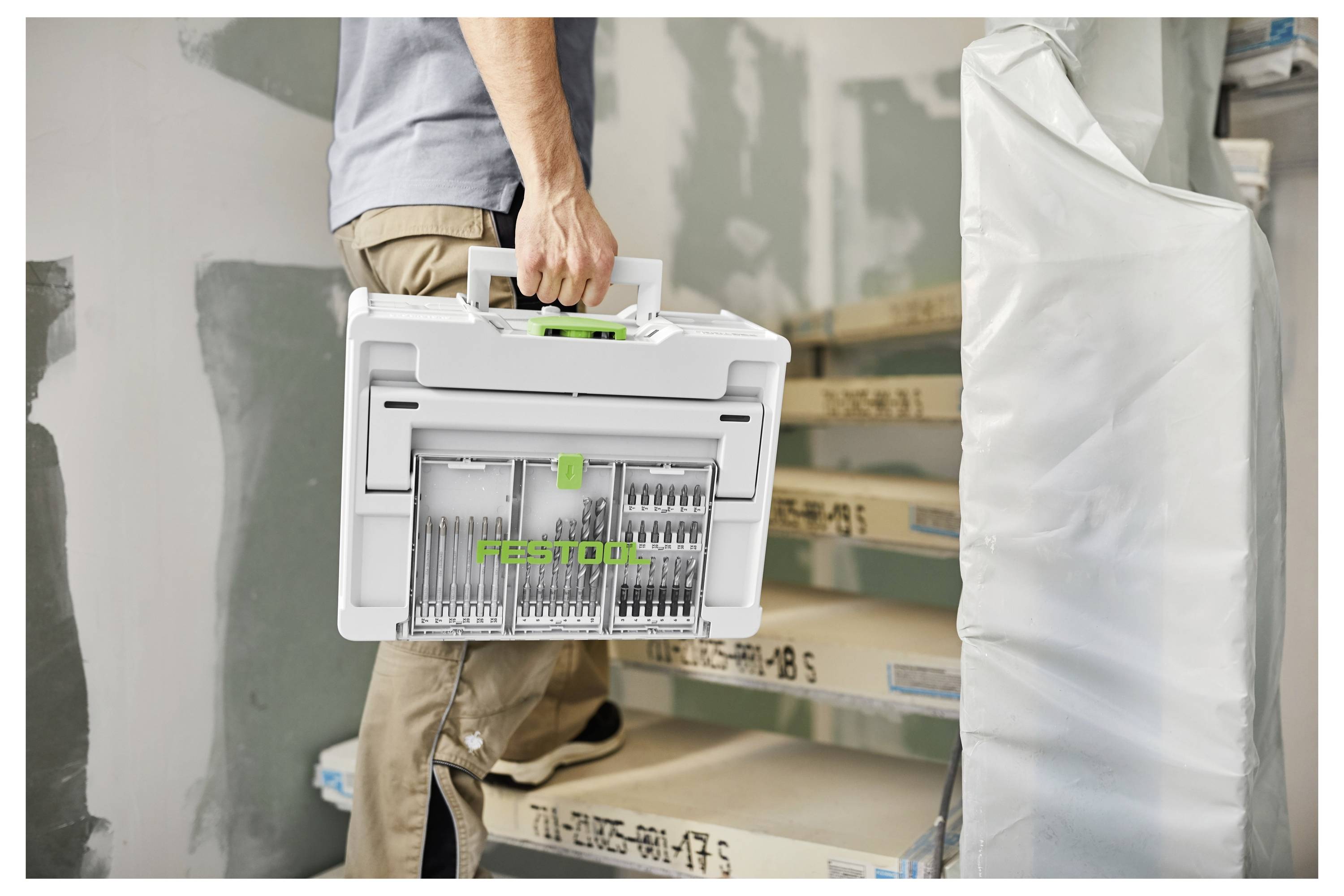 Egy személy fehér Festool szerszámosláda mellett sétál fel egy részlegesen felújított szobában található falépcsokon, és a ládában szerszámok vannak.