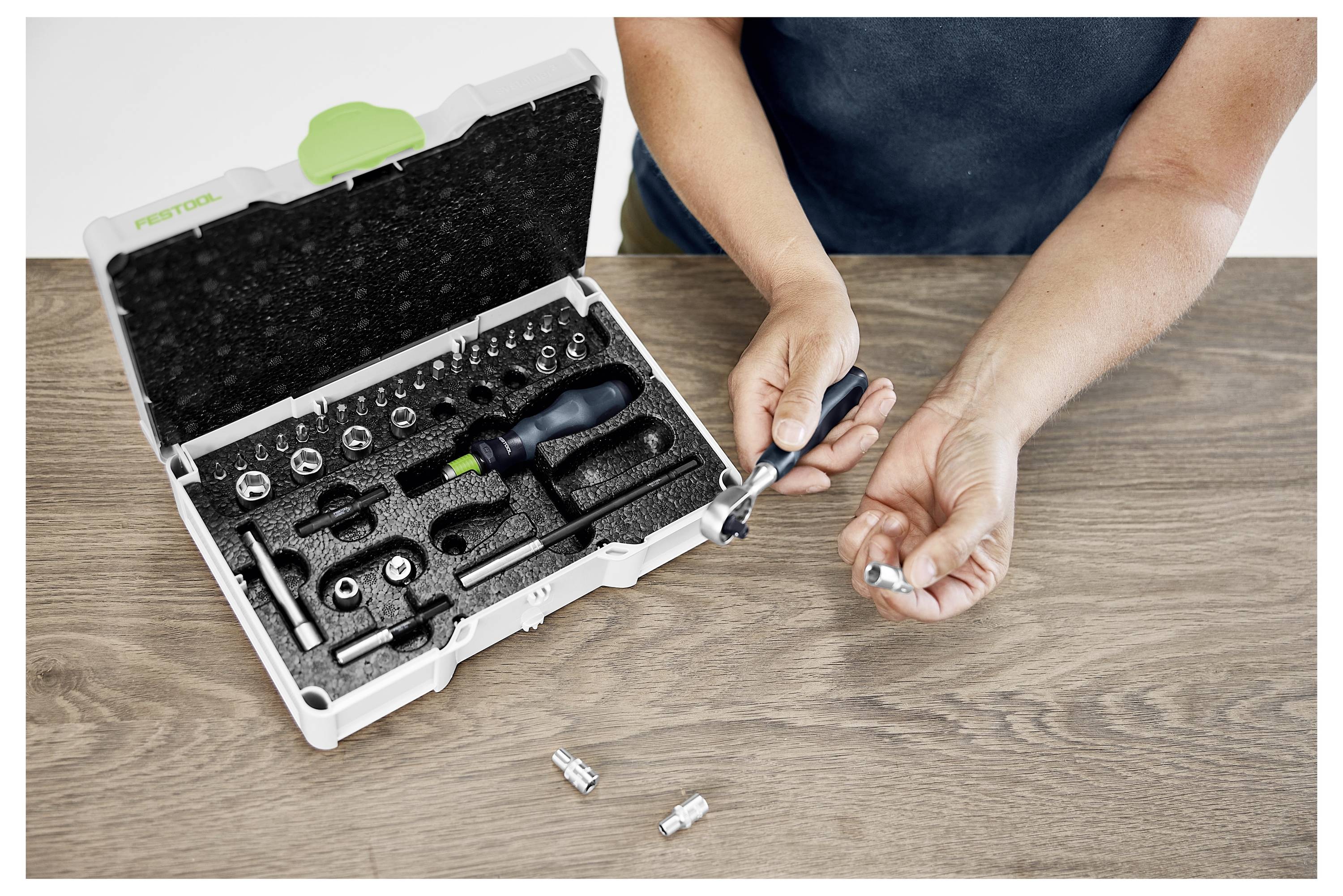 Egy biztonsági szemüveget viselő férfi elektromos szerszámot használ az ablakkereteken való munkavégzéshez egy világos műhelyben.