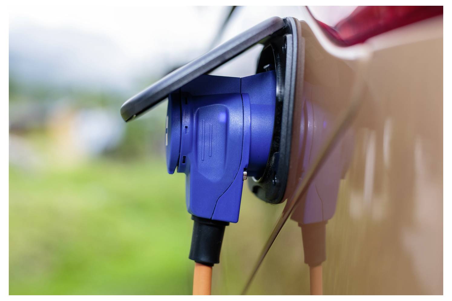 Kék elektromos jármű töltőcsatlakozó csatlakozva egy autó töltőportjához kültéren.