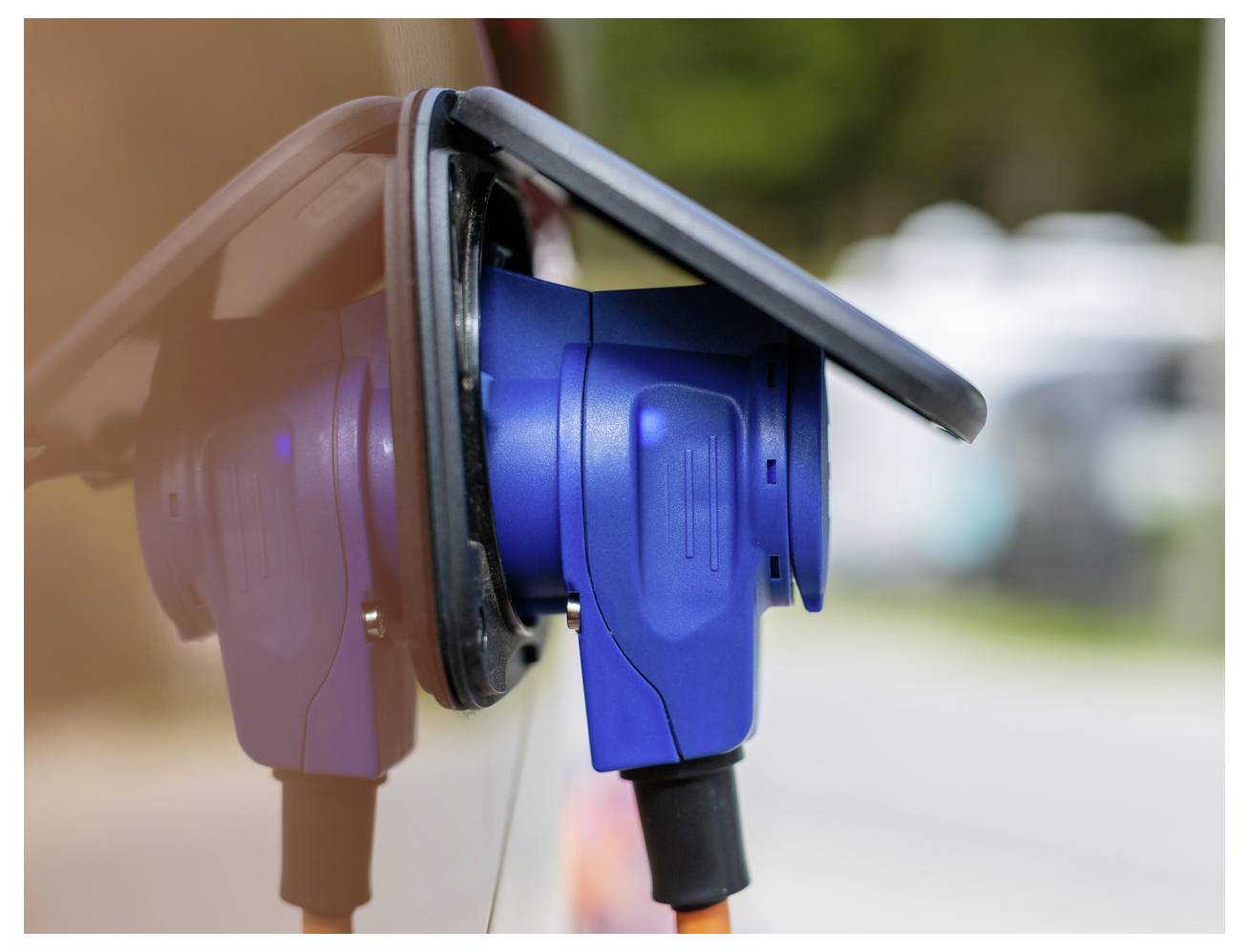 Kék és fekete elektromos járműtöltő csatlakozódugó egy autóhoz csatlakoztatva a töltőállomáson, közeli nézet.