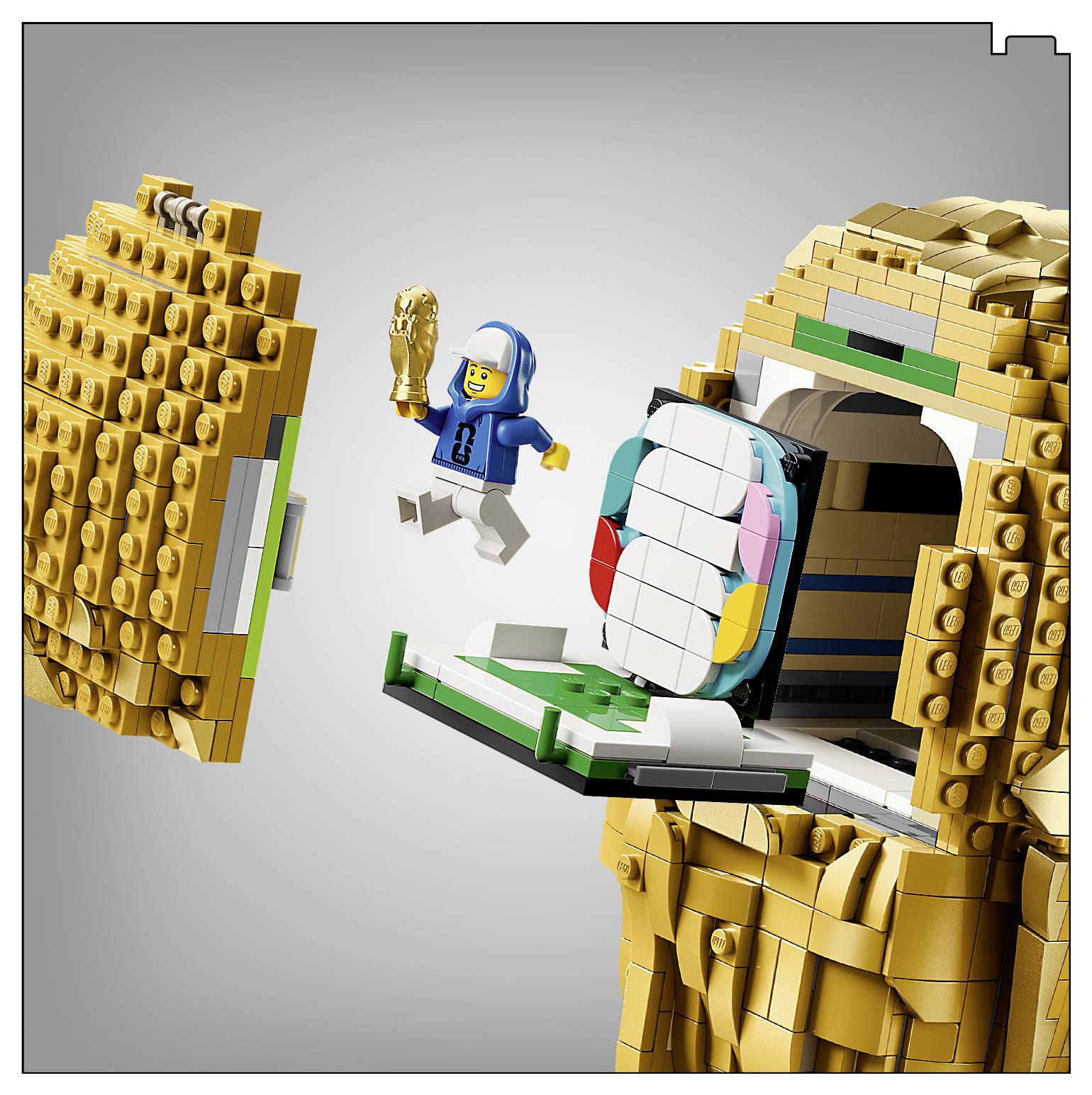 Egy kék kapucnis LEGO figura egy arany alma szerkezetből ugrik le, egy arany trófea tartva a kezében.