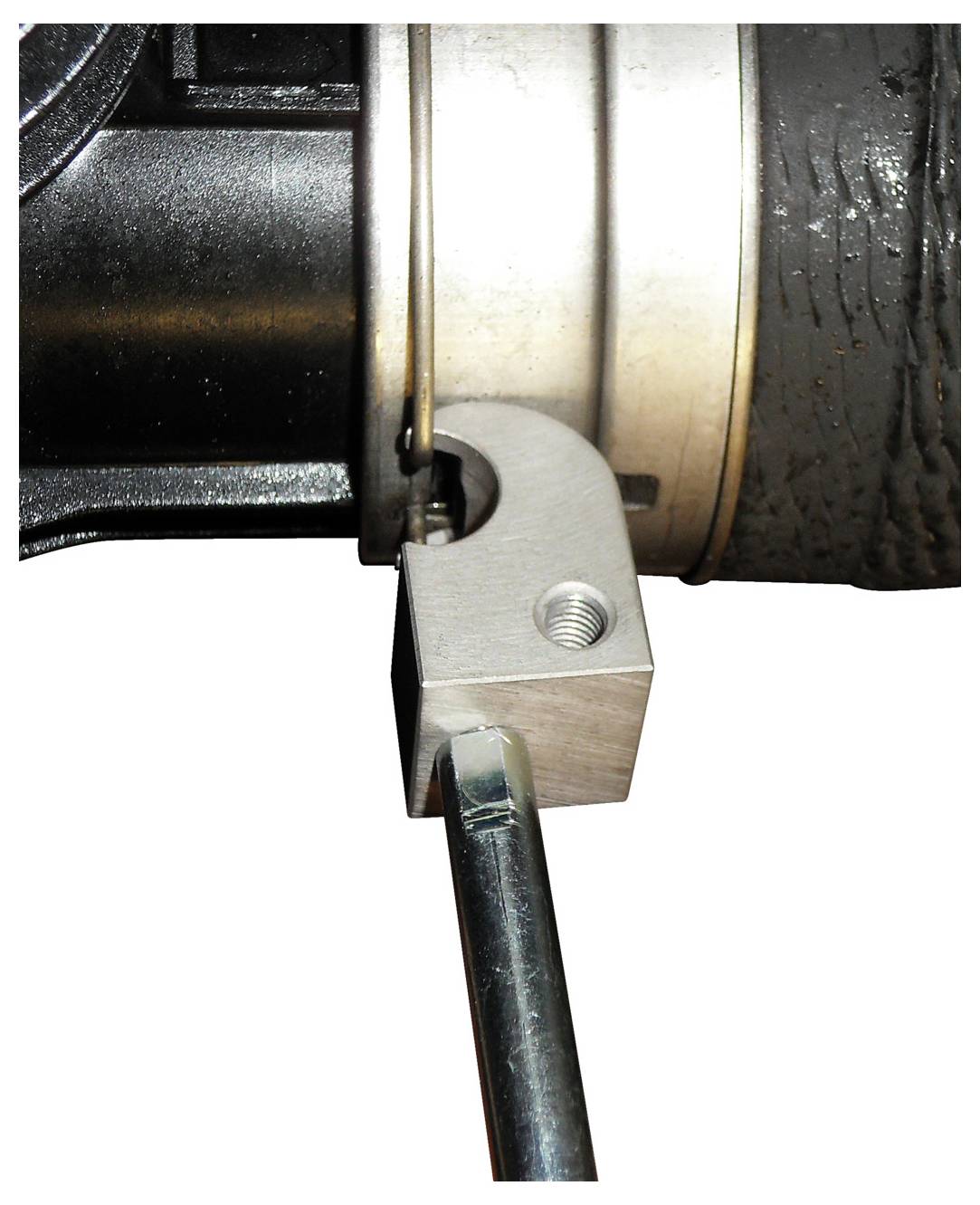 'Egy tömlőbilin egy textúrált tömlőn, hatszögletű csavarral rögzítve egy fém konzolhoz a bal oldalon.'