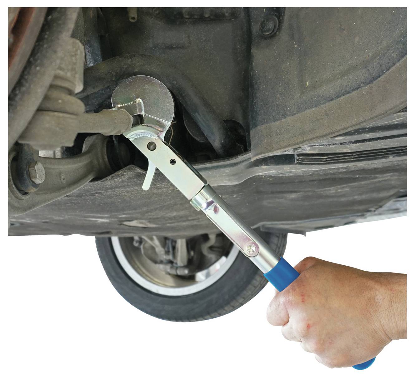 Egy kéz kék nyéllel rendelkező szerszámot használ az autó olajszűrőjének megfogásához eltávolítás vagy felszerelés céljából, a háttérben egy kerék látható.