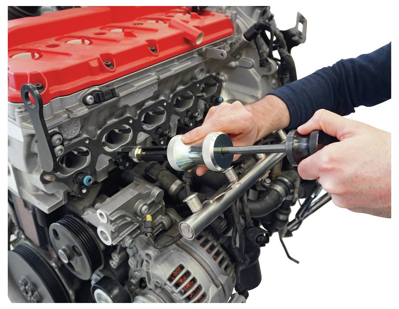 Szerelő szerszámot használ egy nyitott autómotor felett, amelynek piros burkolata és látható dugattyúi vannak, karbantartás vagy javítás végzéséhez.