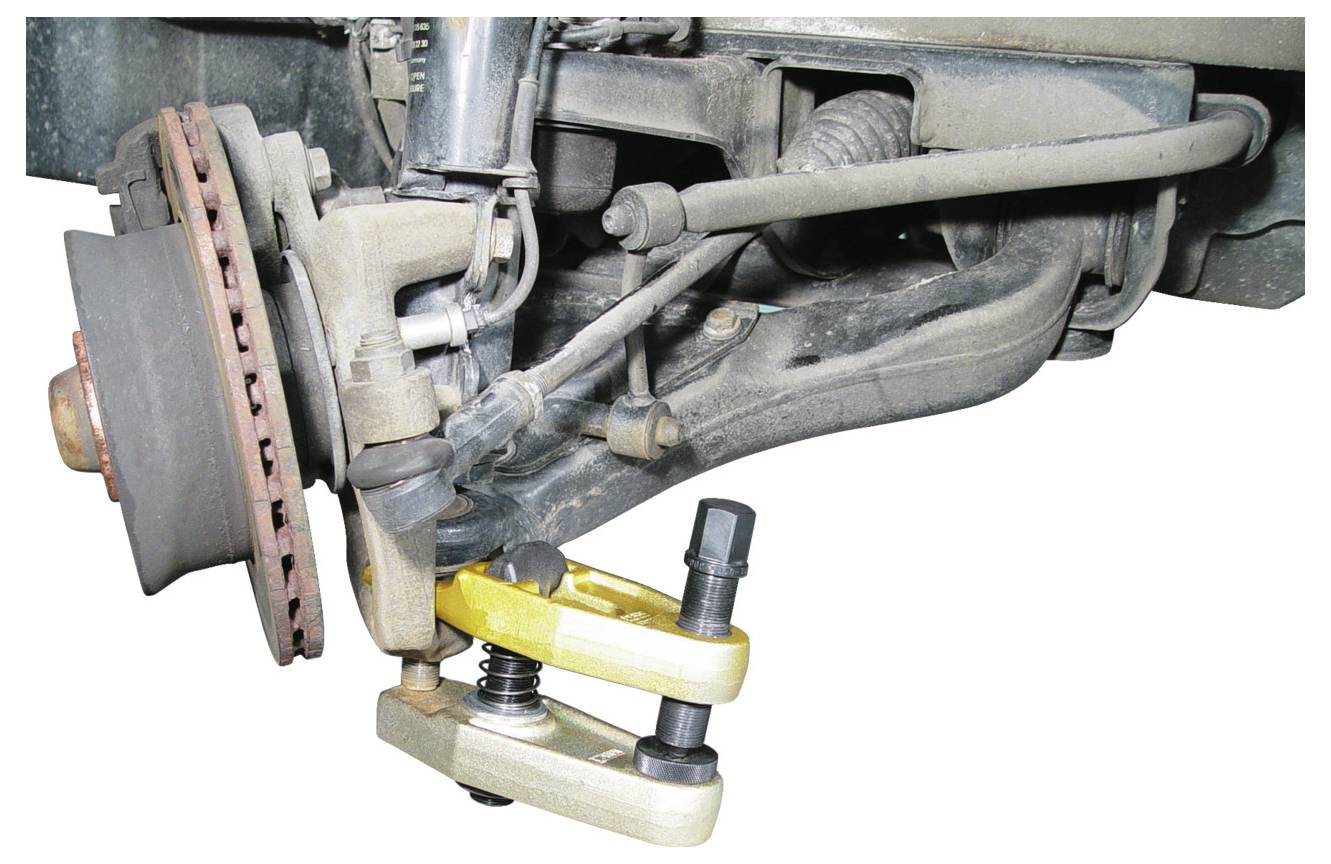 Közeli felvétel egy jármű felfüggesztési rendszeréről, amely egy gömbcsapágy-elválasztó eszköz használatát mutatja be, demonstrálva a jármű karbantartását vagy javítását.