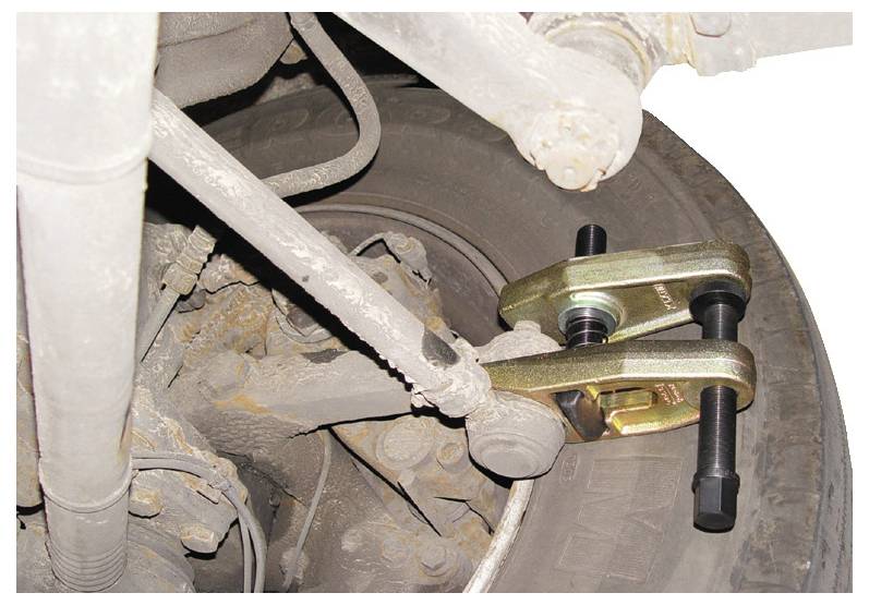 Egy jármű felfüggesztési rendszere egy golyócsukló-elválasztó szerszámmal felszerelve, amely a mechanikus alkatrészek és rozsdás területek közeli képét mutatja.