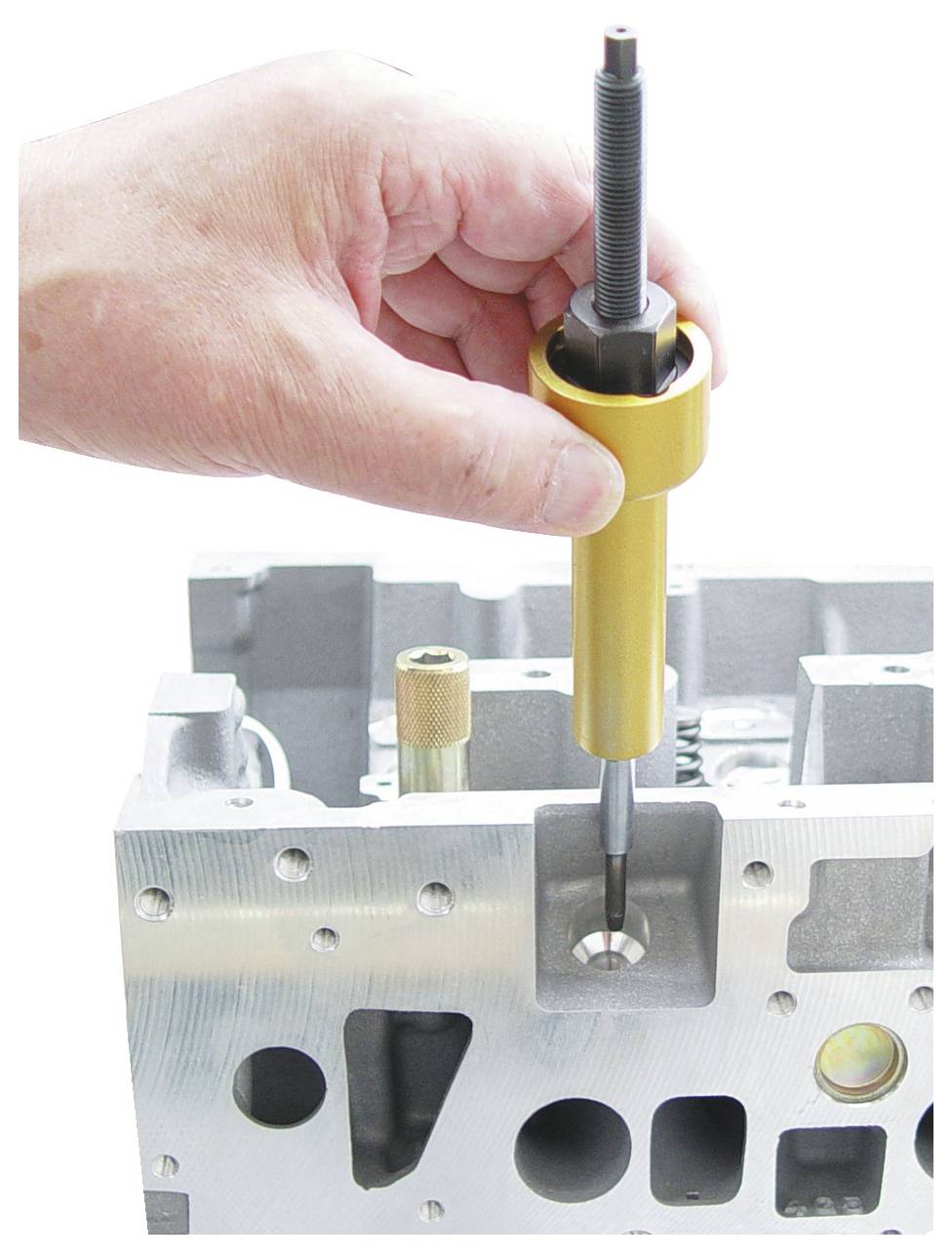 'Kéz, amely egy szerszámot használ szelepvezető telepítéséhez egy autómotor blokkban.'