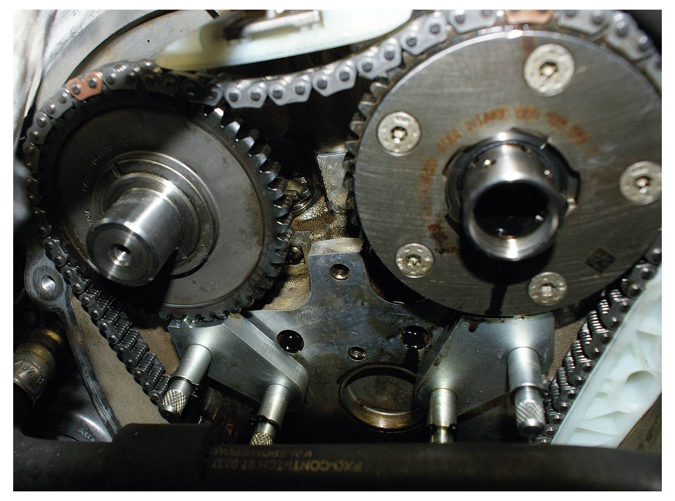 Autómotor időzítési lánc szerelvényének közeli nézete, fogaskerekek és láncok összekapcsolódásával, amely a mechanikus szerkezetet emeli ki.