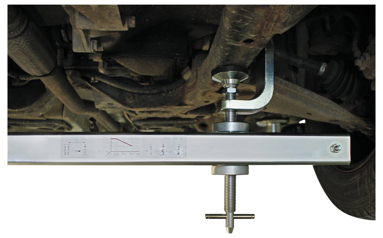 Egy autó alsószerkezete, keresztgerendával és állítható szorítószerszámmal felszerelve, valószínűleg alkatrészek mérésére vagy igazítására szolgál.