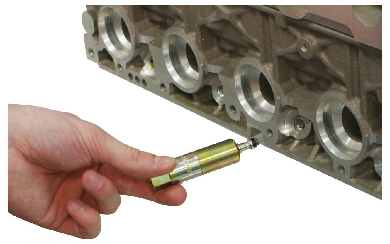 Egy kéz egy kis hengeres szerszámot használ a motor blokkjának szelepvezetékeinek igazításához. A szerszám pontosan illeszkedik, ami karbantartásra vagy összeszereléséről tanúskodik.