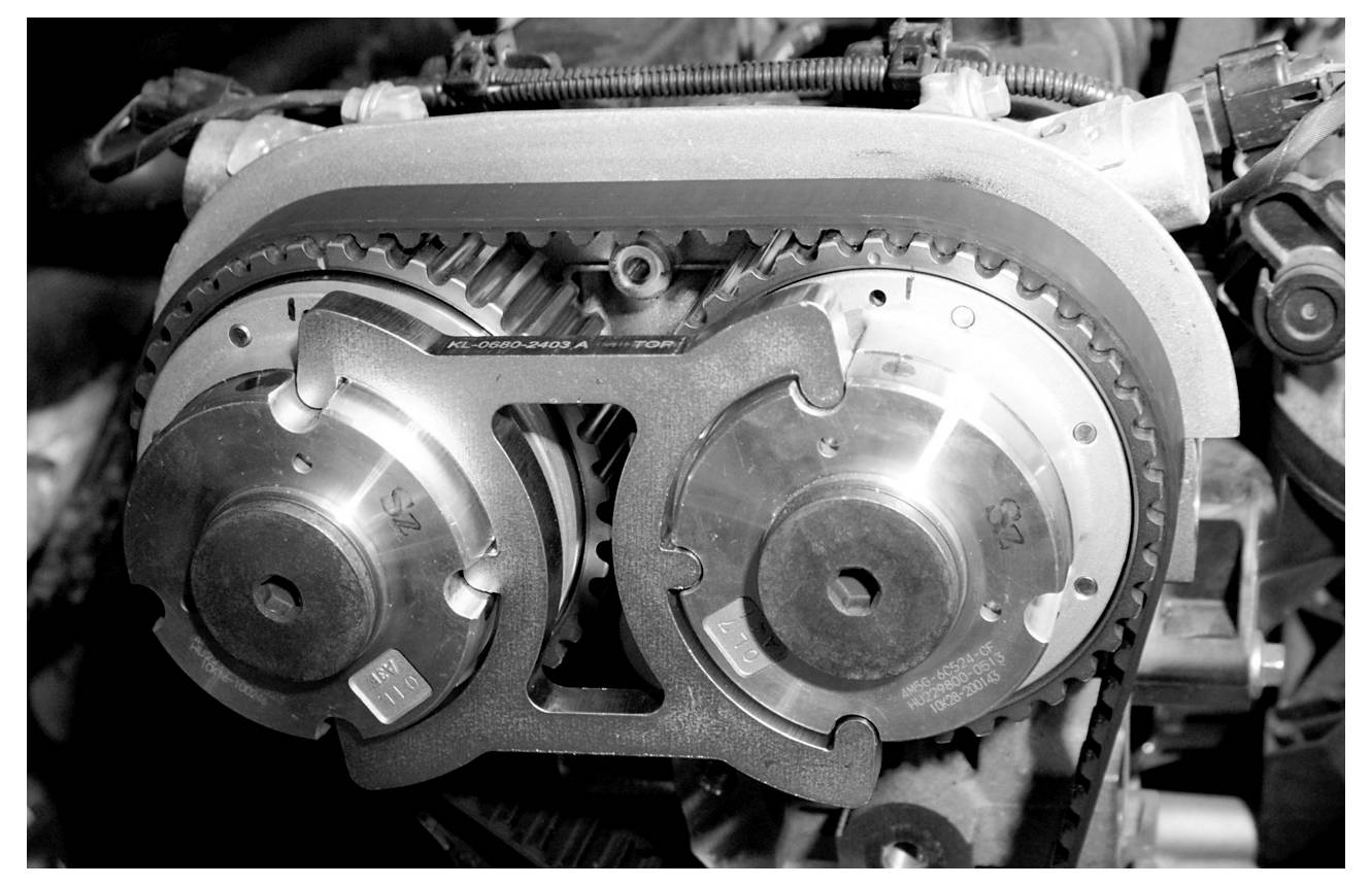 Egy motorvezérlési rendszer fekete-fehér nagyítása, amely két nockatengelyt és egy vezérlőszíjat mutat, kiemelve a mechanikai pontosságot.