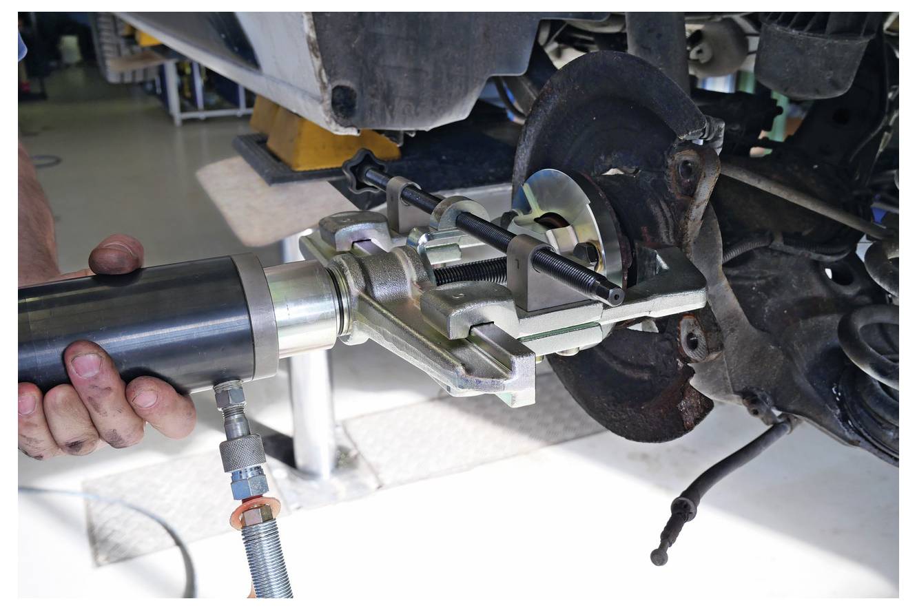 Egy autó kerékagy lehúzó berendezés látható használatban, amelynél hidraulikus eszköz nyom ki az agy eltávolításához járműkarbantartás során.