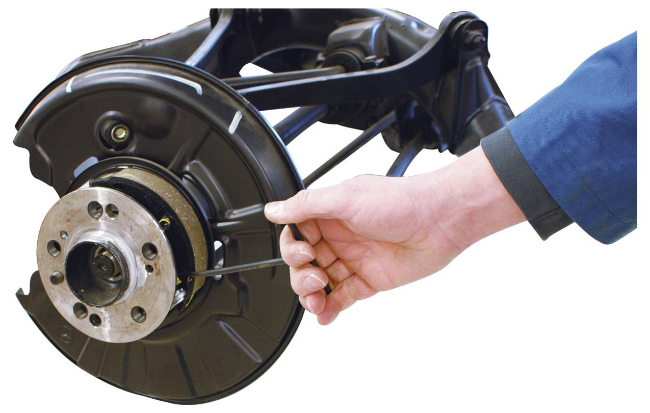 Egy kéz fékezési beállító szerszámot tart egy jármű féktárcsájánál, amely fékezési beállítást mutat be.