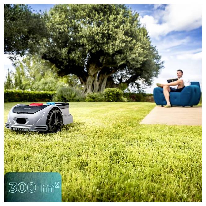 Egy robotfűnyírógép működik egy füves gyepen egy nagy fa közelében, a háttérben pedig egy személy ül egy széken kék ég alatt.