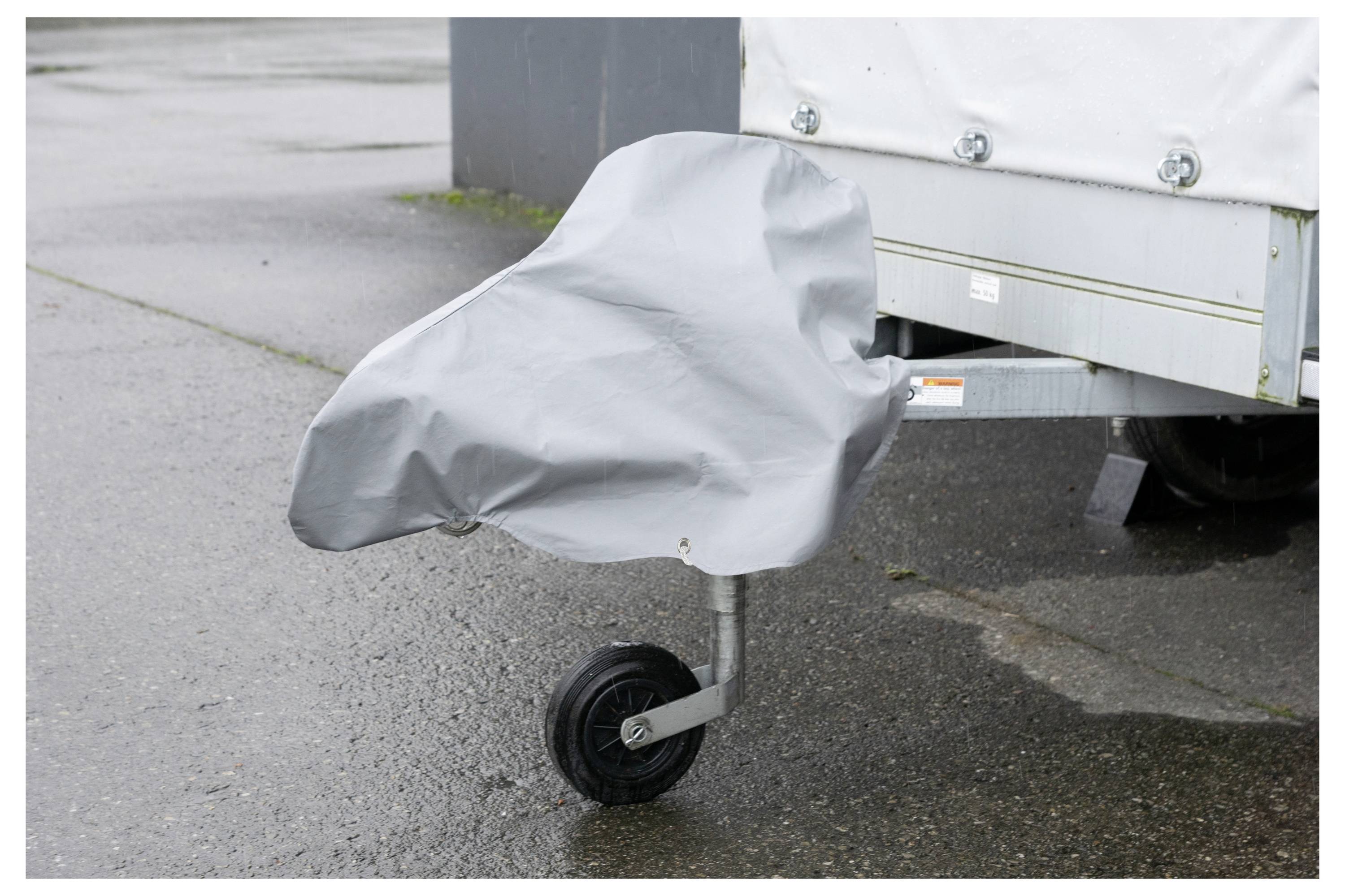 Egy pótkocsit képez le vizes aszfalton fedett kerékkel, amely esős időjárás elleni védelmet sugall.