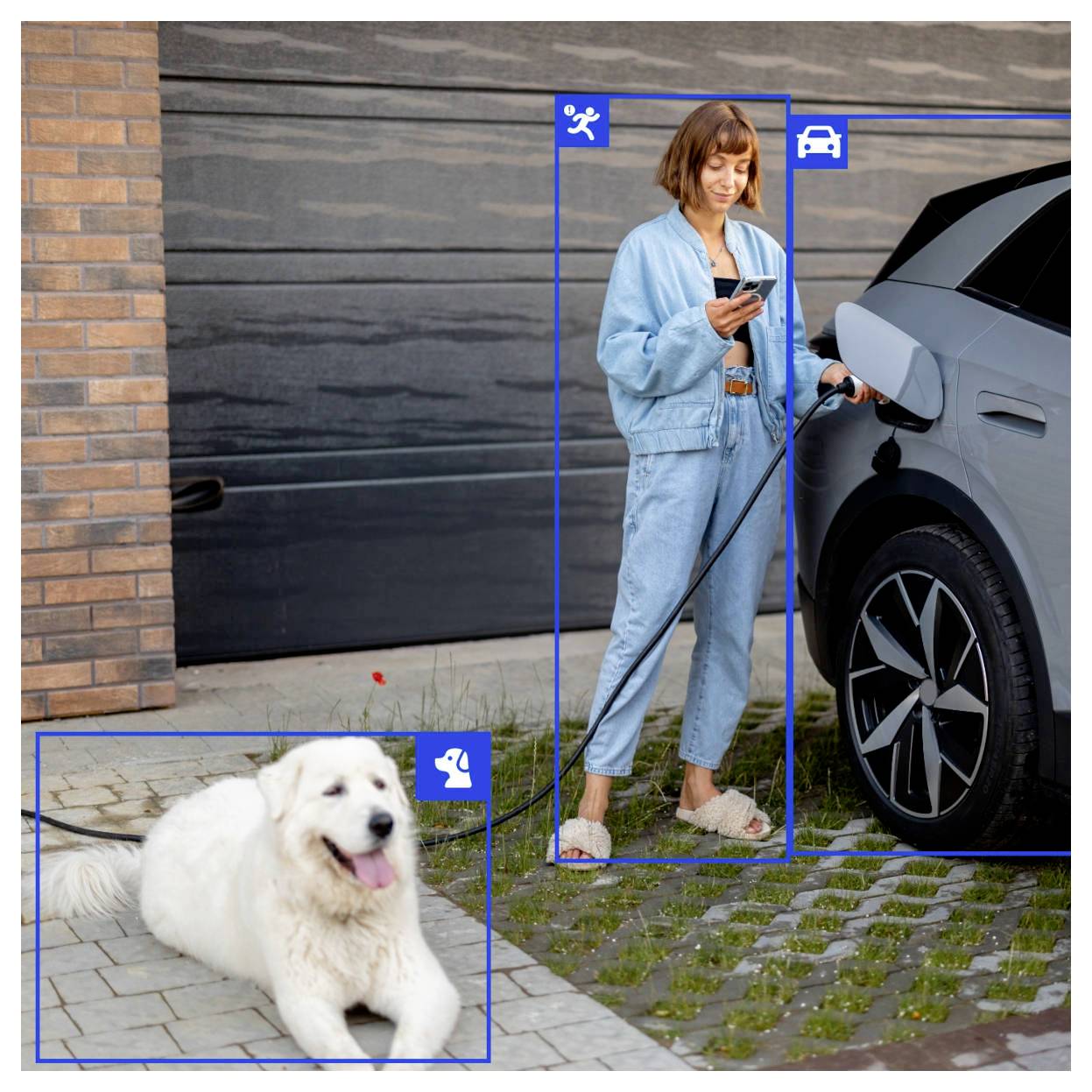 Egy kék ruhában lévő személy telefonját tartva egy elektromos autót tölt. A közelben egy bozontos fehér kutya fekszik a földön.