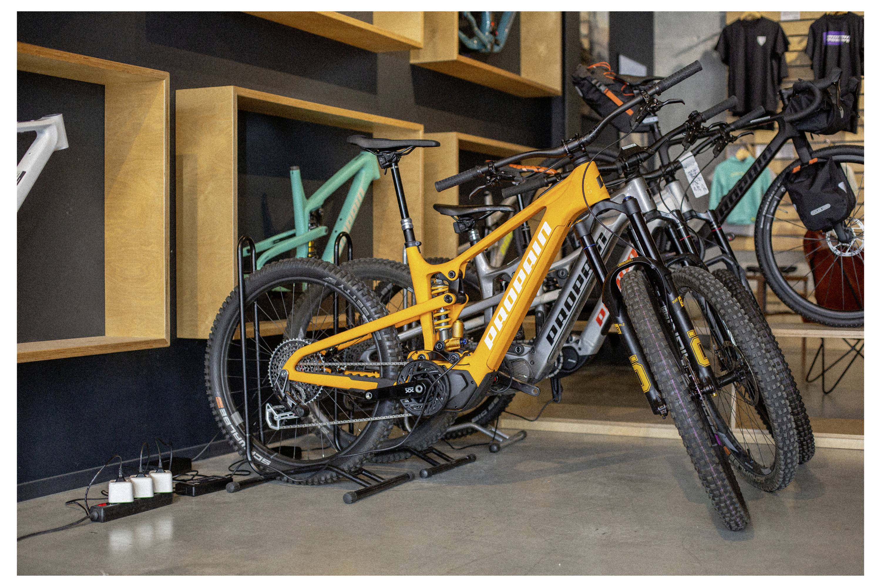 'Narancssárga e-bike kiállítva egy bemutatóterem padlóján, más biciklik között, a hangsúly a sleek dizájnján és élénk színén.'